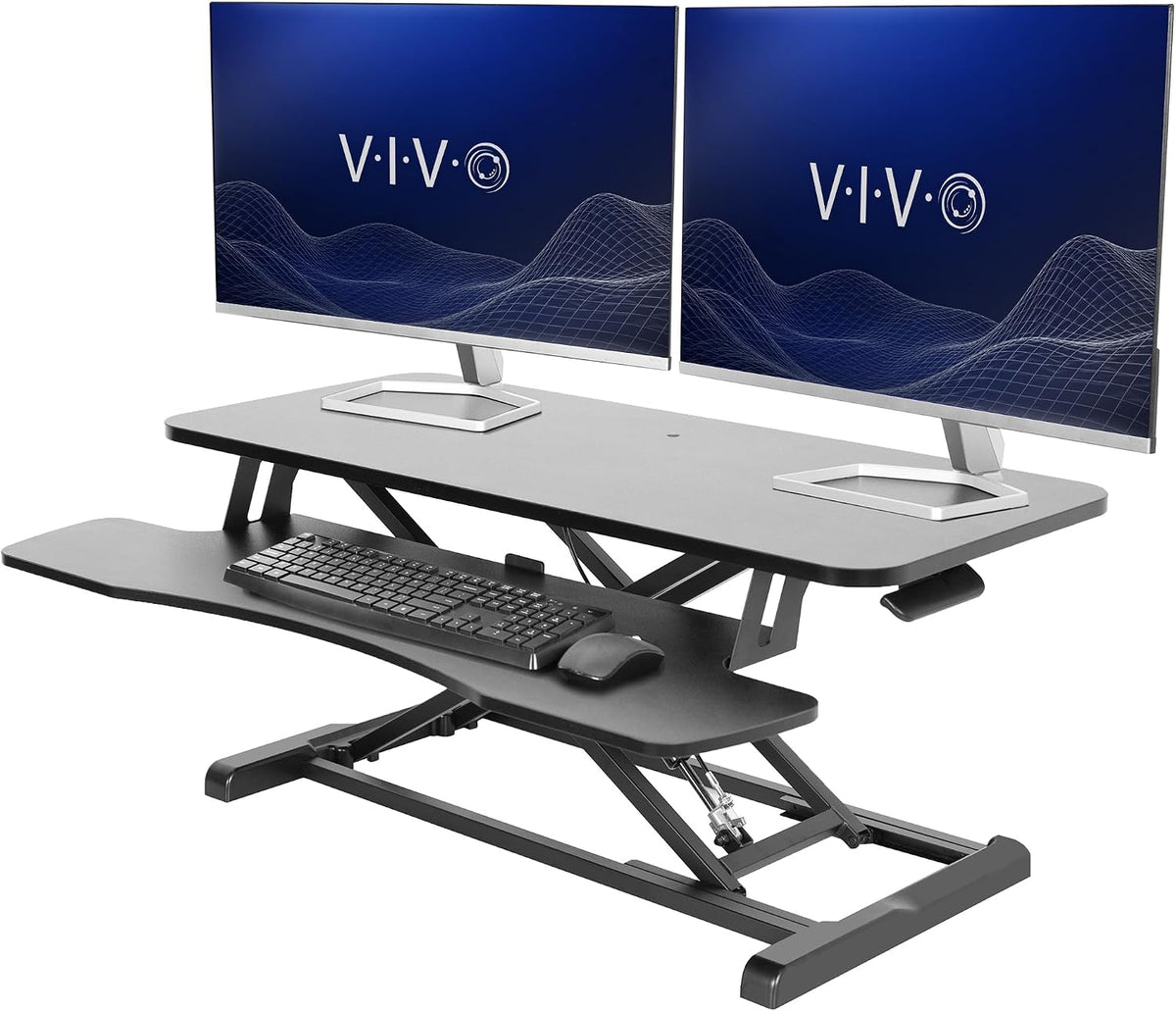 Black standing desk converter staged with dual monitors, keyboard and mouse on the keyboard shelf.