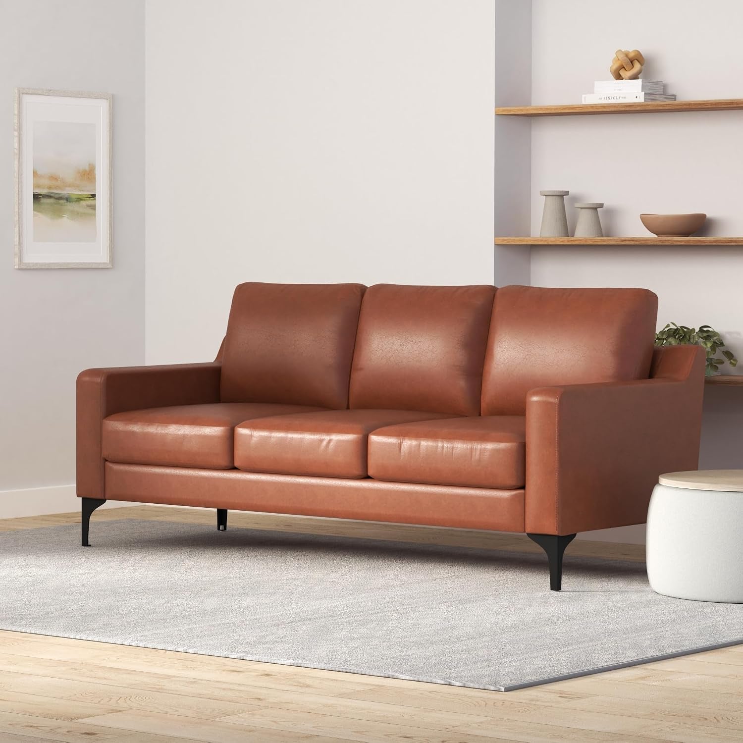 Brown faux-leather sofa angled three-quarter view in a minimalist room showing tapered legs and arm profile