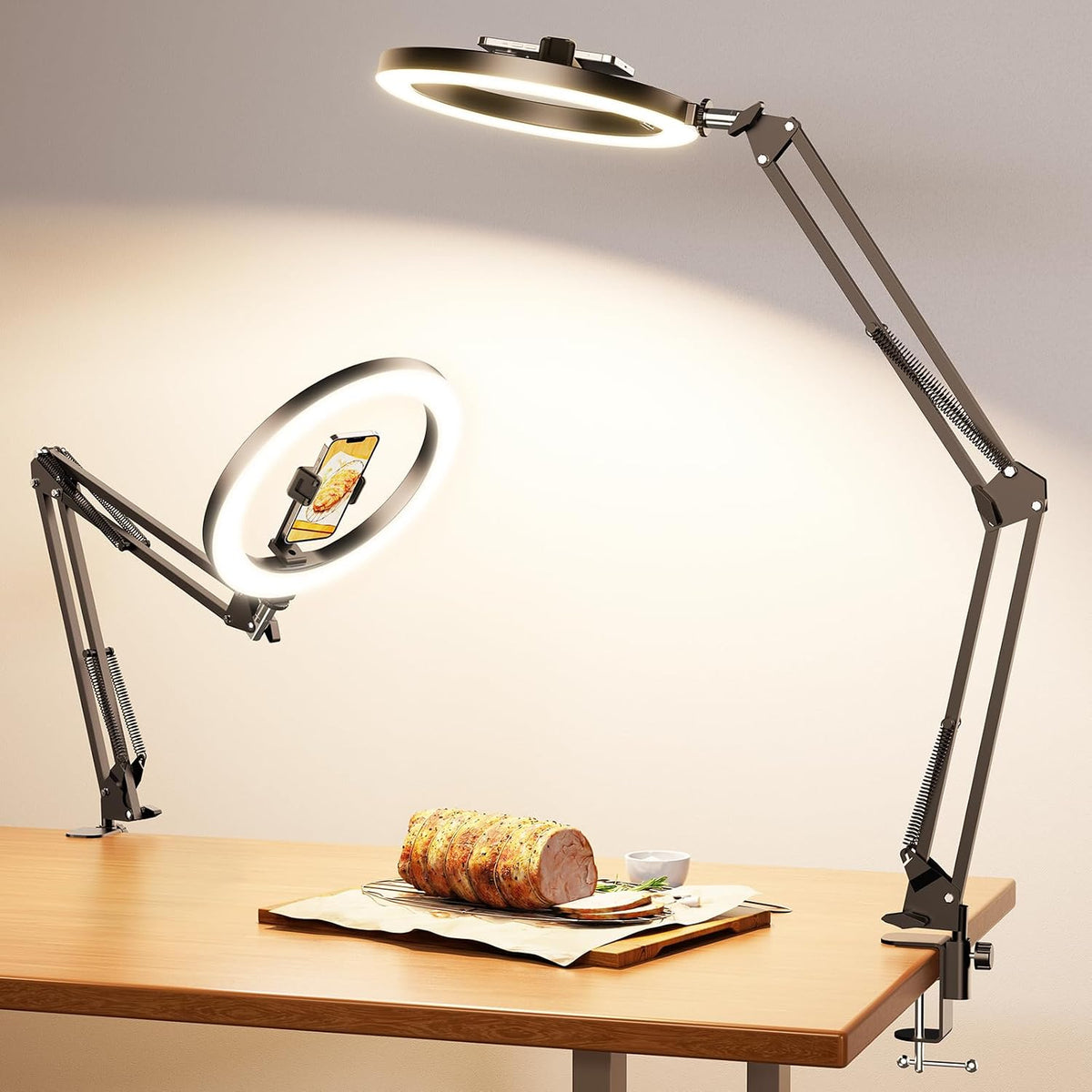 Clamp-mounted adjustable arm with lit ring light and phone holder positioned over a wooden tabletop.