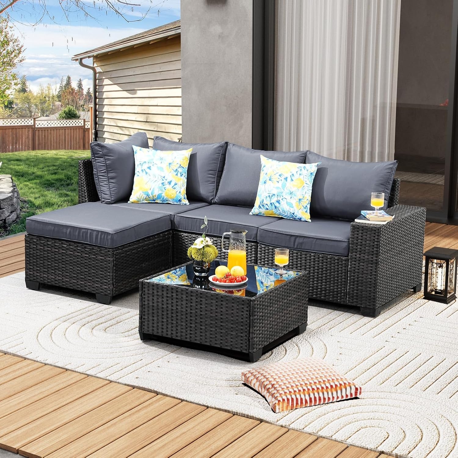 Outdoor arrangement showing dark gray-cushioned sectional, ottoman and square glass-top coffee table.