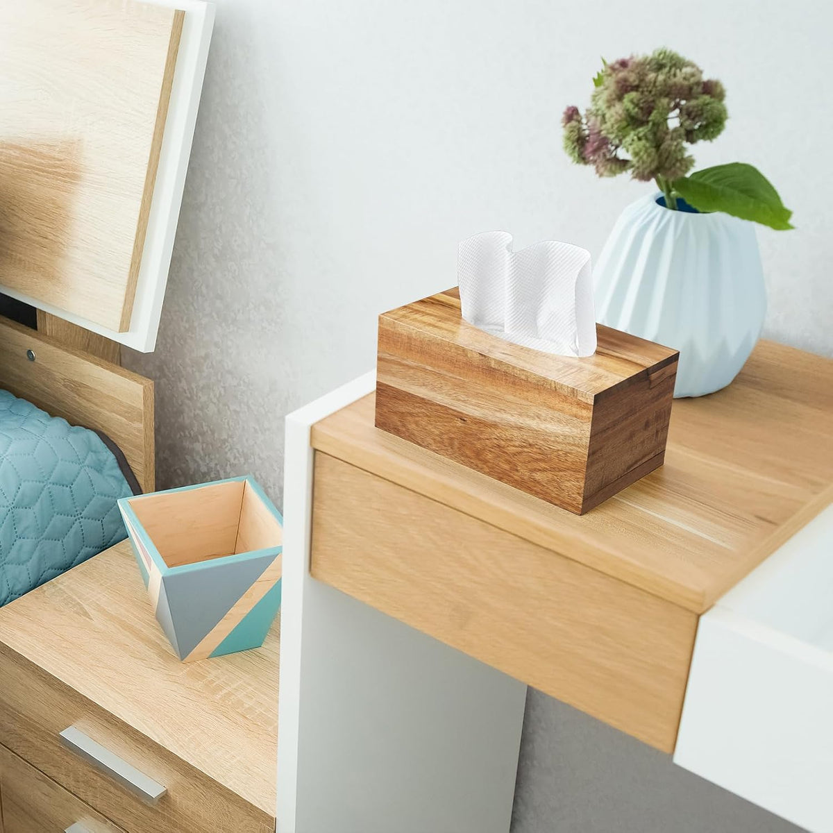 Rectangular acacia tissue cover on a bedside table next to a blue vase and geometric cup.