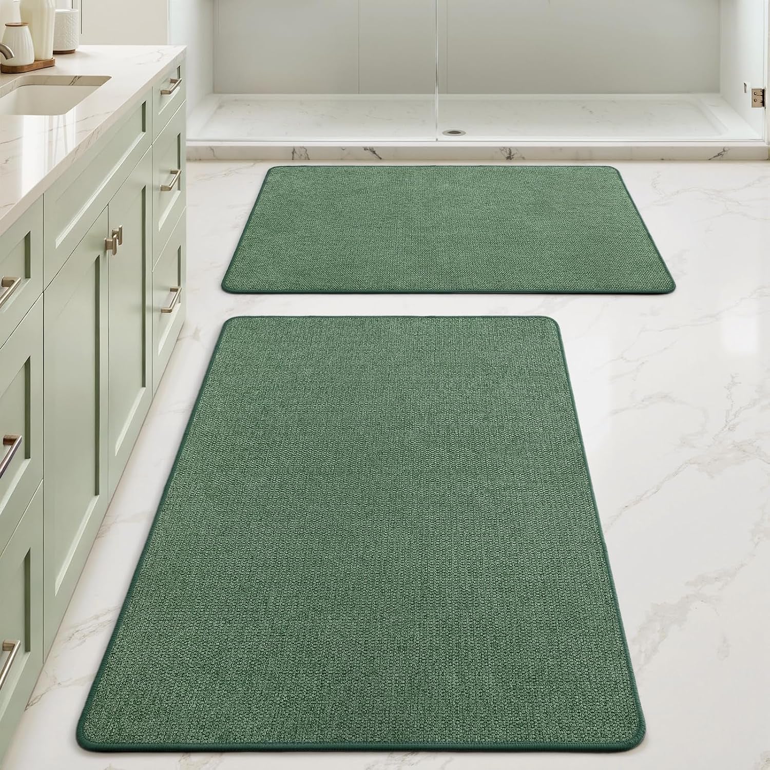 Two green rectangular bath rugs aligned down a bathroom floor beside a light green vanity.