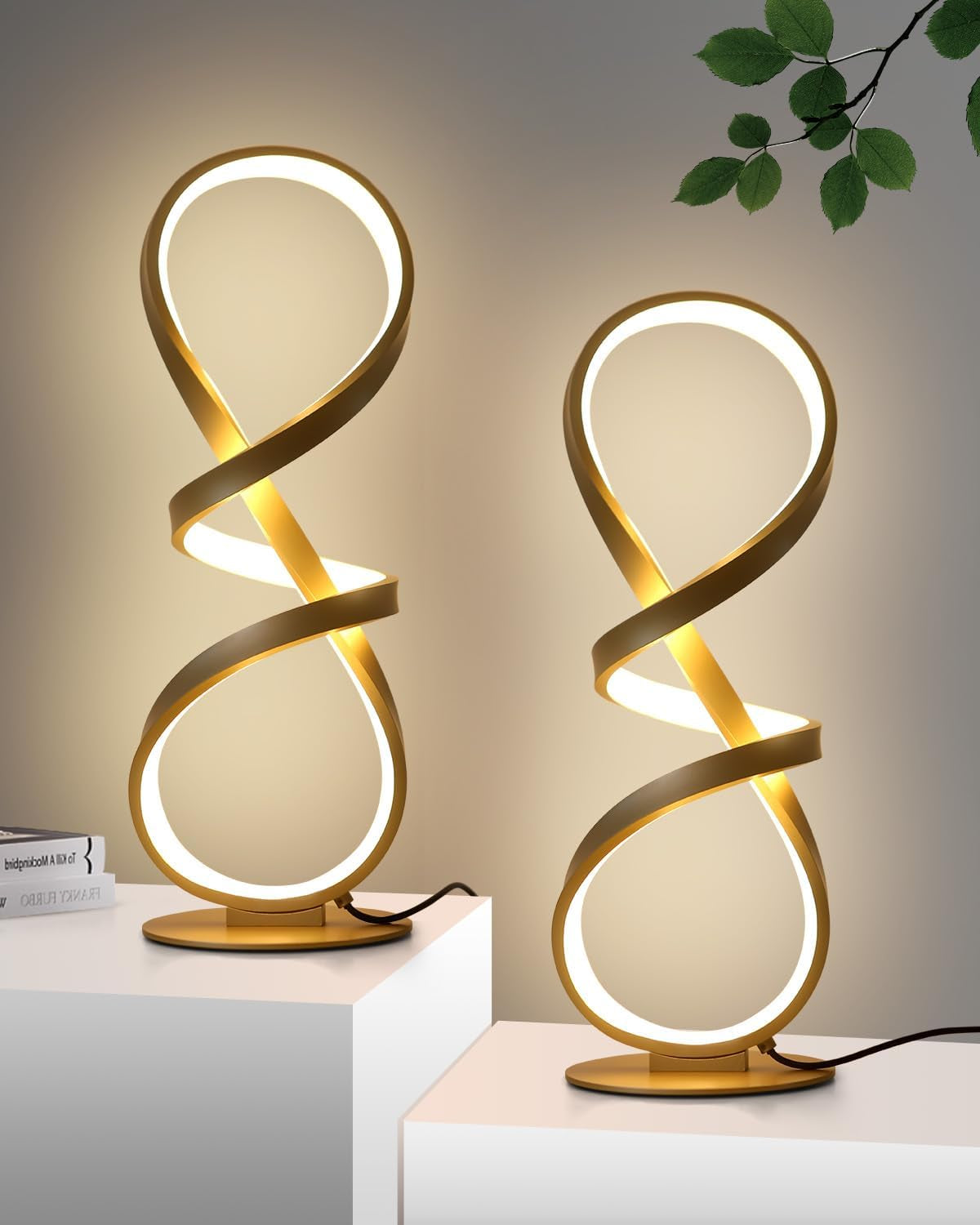 Pair of gold spiral LED table lamps shown side-by-side against a neutral wall, close crop of their infinity loops.