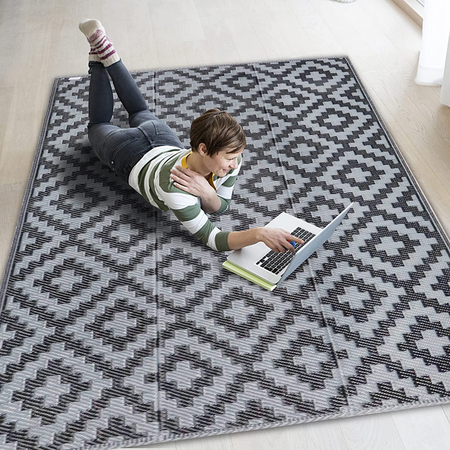 Person lying on a gray patterned rug on a light wood floor using a laptop.