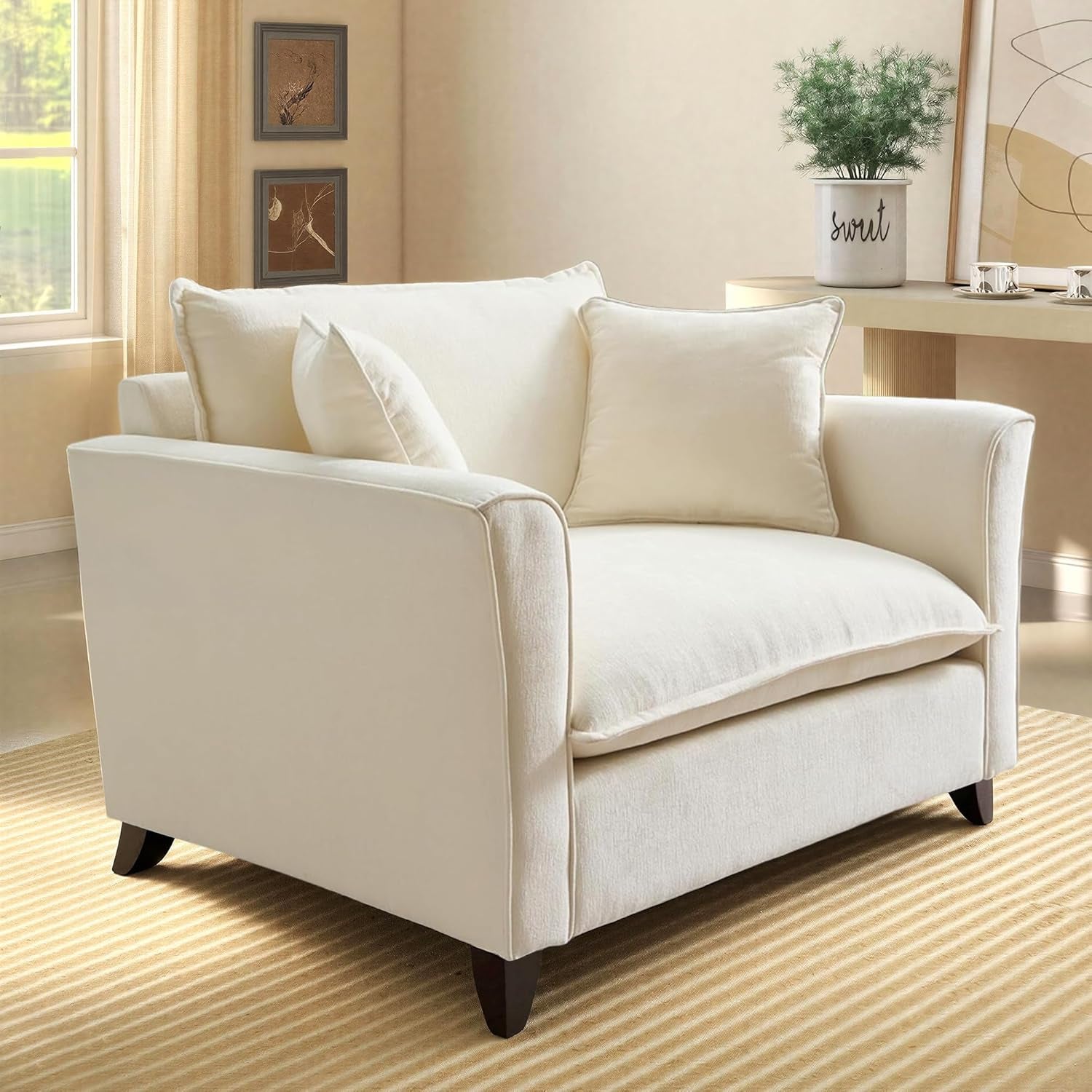 Three-quarter left-side view of a cream oversized accent chair showing curved arms, seat cushion, and dark tapered wooden