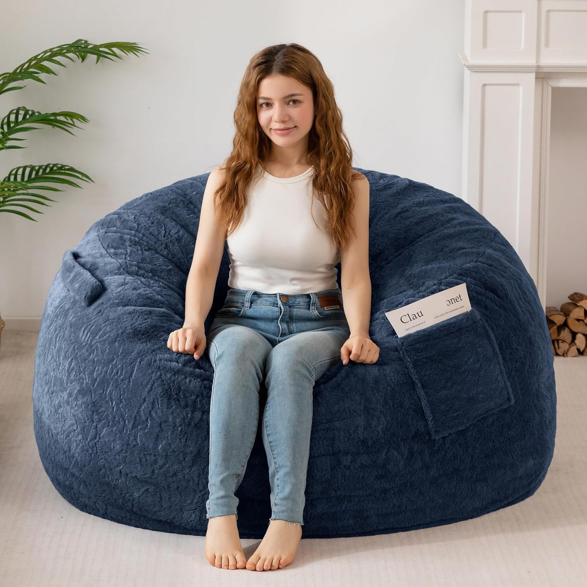 Front view of a navy faux-fur bean bag with a woman seated, showing a side pocket and plush surface