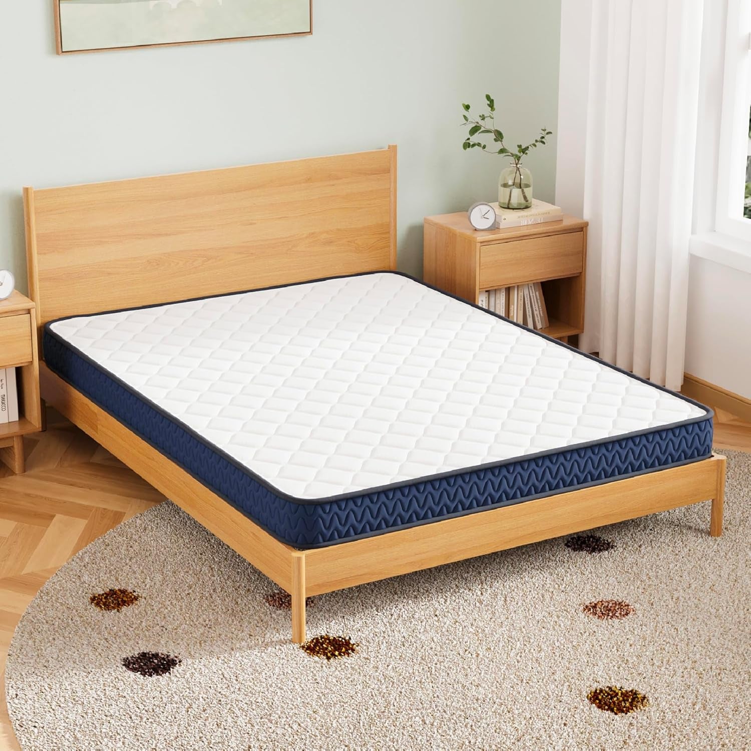 Queen mattress with white quilted top and navy side panel on a light wood platform in a sunlit bedroom.