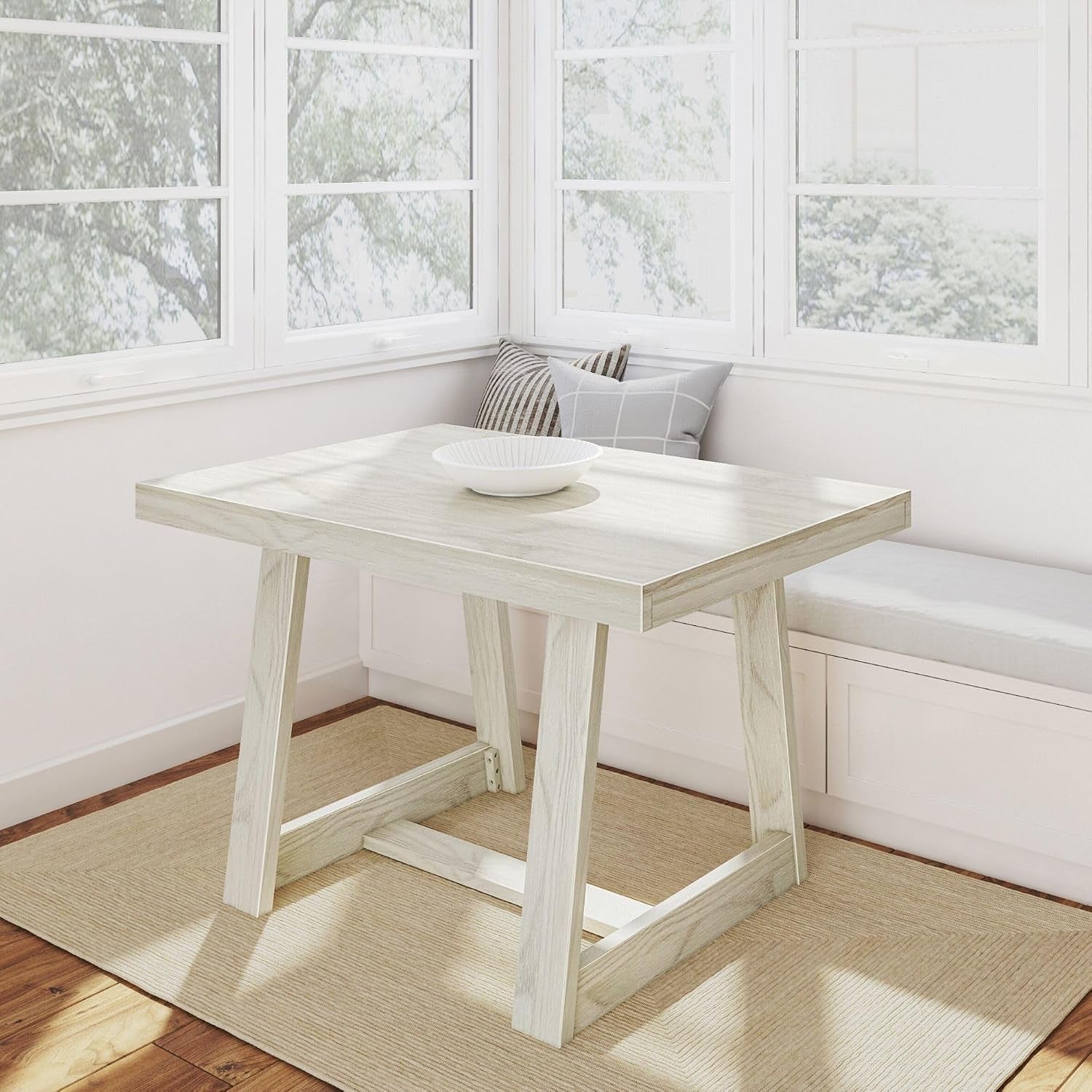 Whitewashed rectangular pine table by a window with bowl and cushioned bench