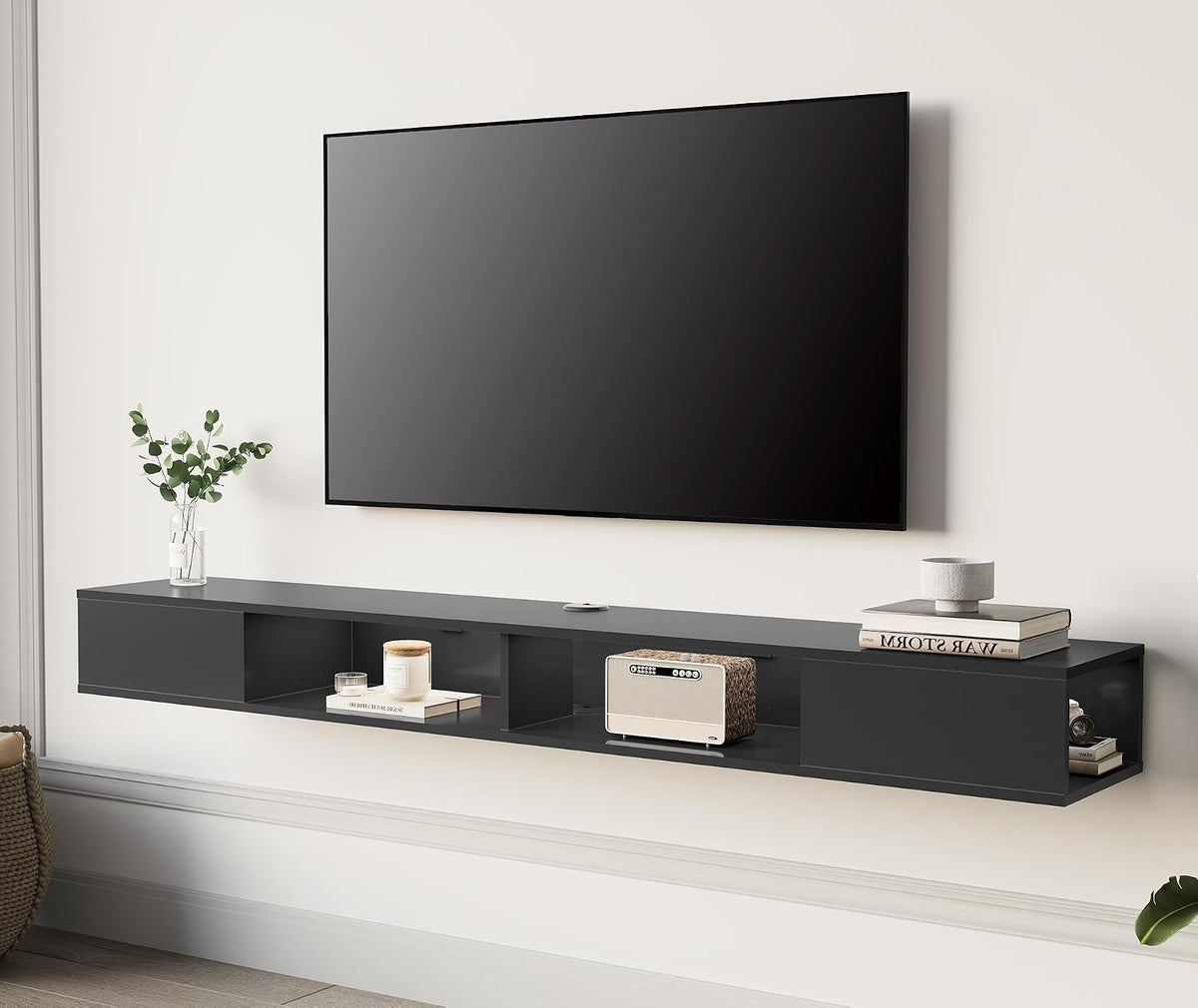 Matte black floating shelf mounted under a wall TV, styled with a small speaker, vase, books and a candle on top.