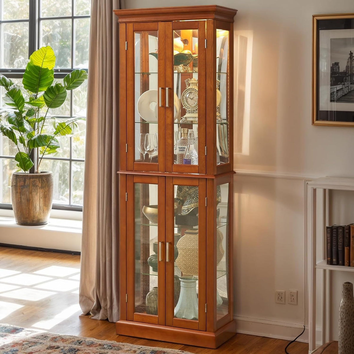 Honey-toned curio cabinet near a sunlit window and potted plant, with its interior lights on and a visible floor cord.