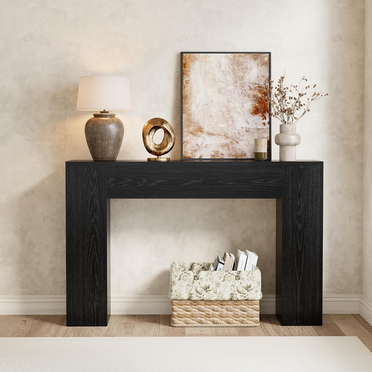 Front view of a charcoal black wood console table styled with a lamp, circular sculpture and leaning artwork.