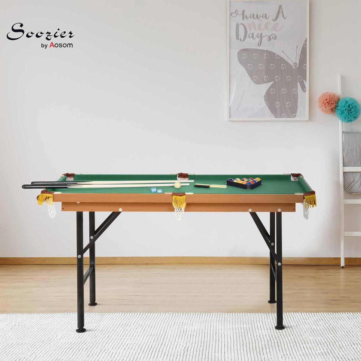 Front view of mini pool table in a bright room with green playing surface, cues and triangle rack