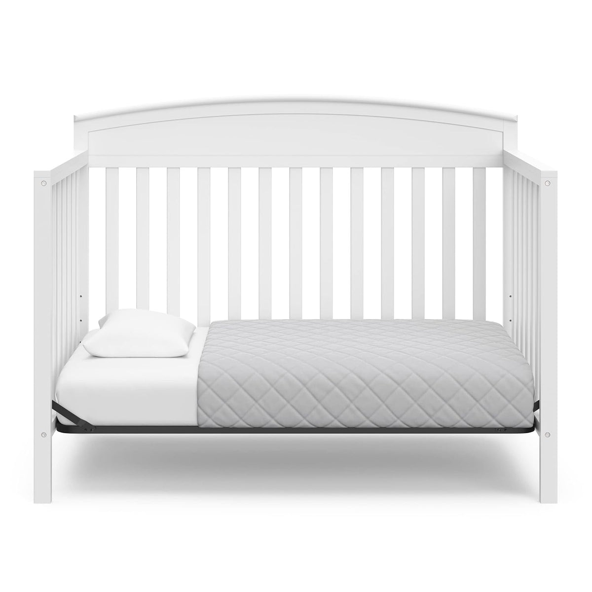 Front view of the crib set up as a toddler bed with a low mattress, quilted blanket and a pillow.