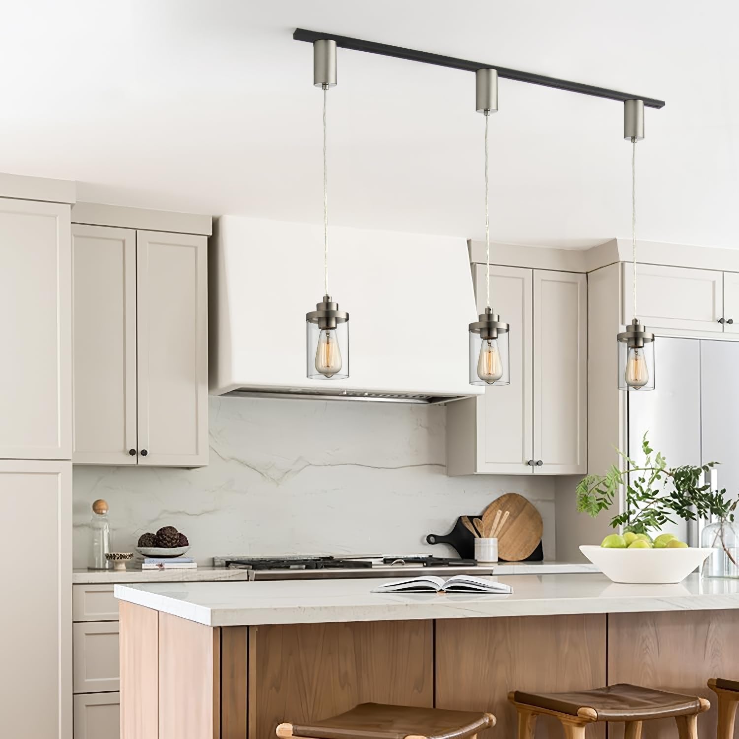 Kitchen island lit by three brushed-nickel track pendants with clear glass shades suspended from a black H-type track