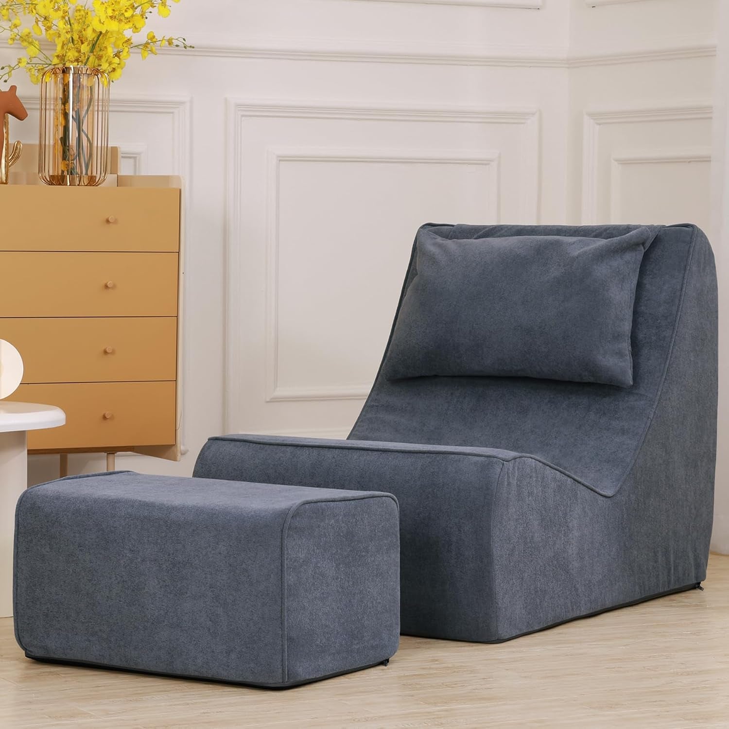 Close-up side view of a dark blue-gray chaise lounge and ottoman on a hardwood floor