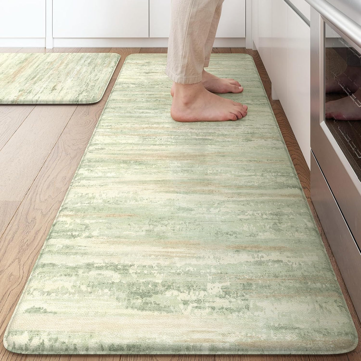Top view of a green-toned abstract kitchen mat with feet standing near a cabinet and oven.