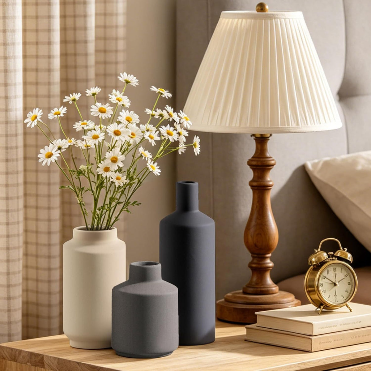 Matte ceramic vases styled on a bedside table next to a wooden lamp, daisies and an alarm clock, lifestyle shot