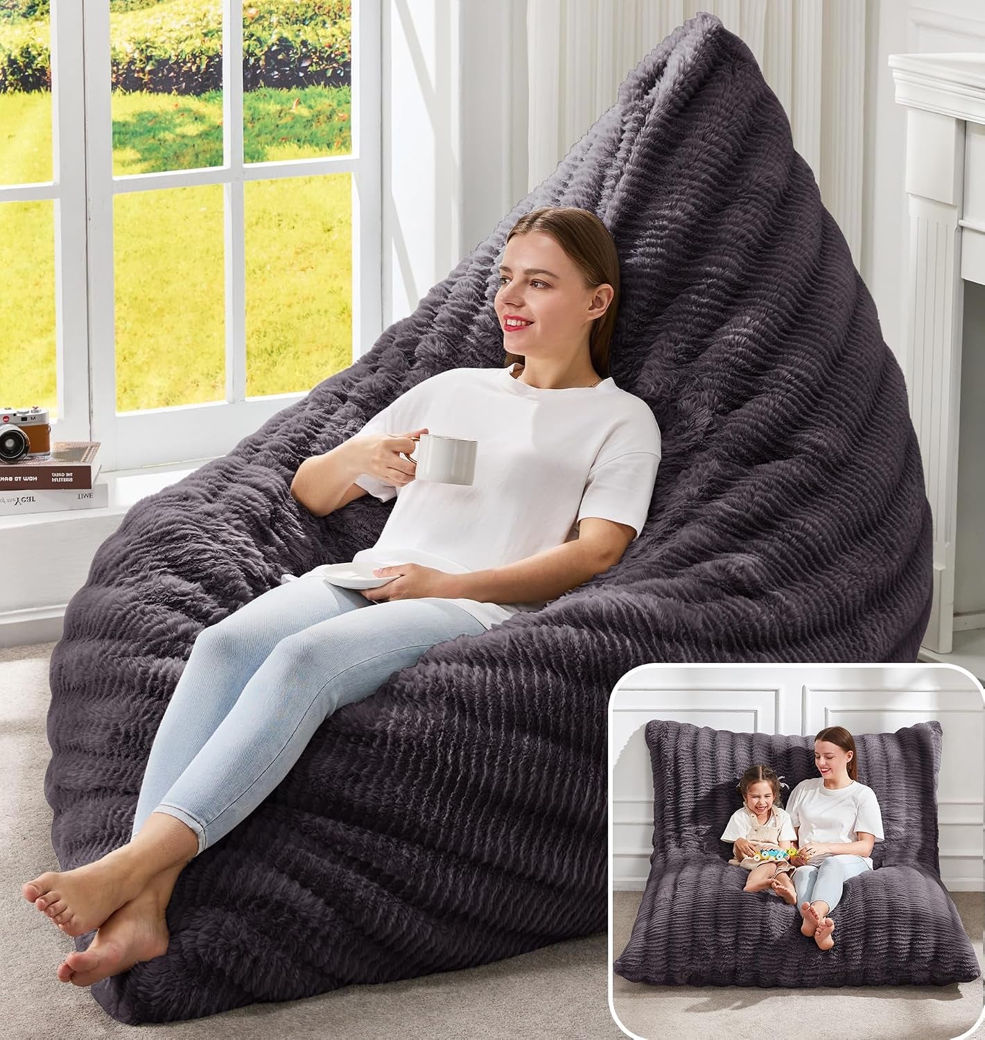 Woman reclining on a large textured dark charcoal memory-foam bag chair near a window, holding a mug.