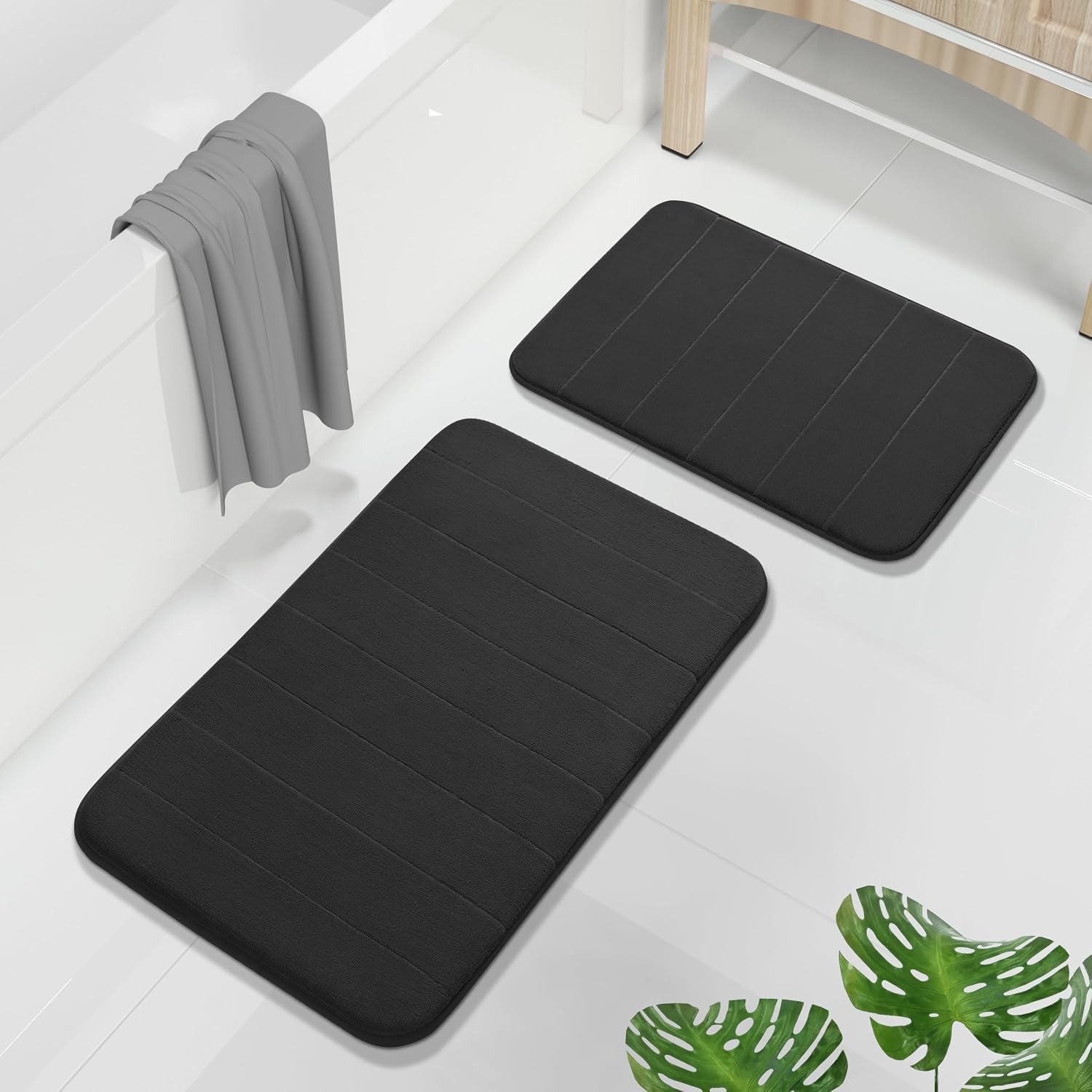 Black rectangular bath mats arranged near a bathtub with a gray towel draped over the tub