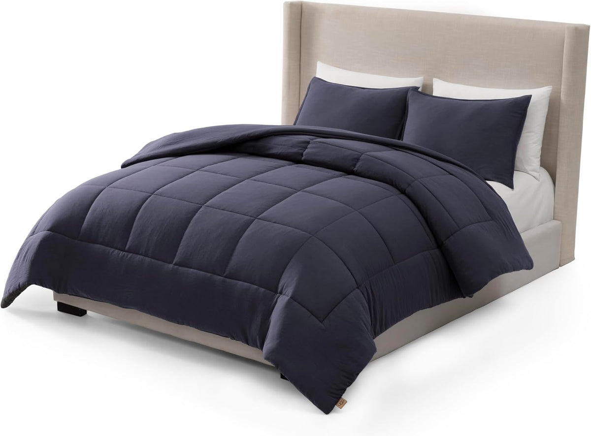Deep navy box‑stitched comforter on a styled bed shown from the lower corner with one sham visible.