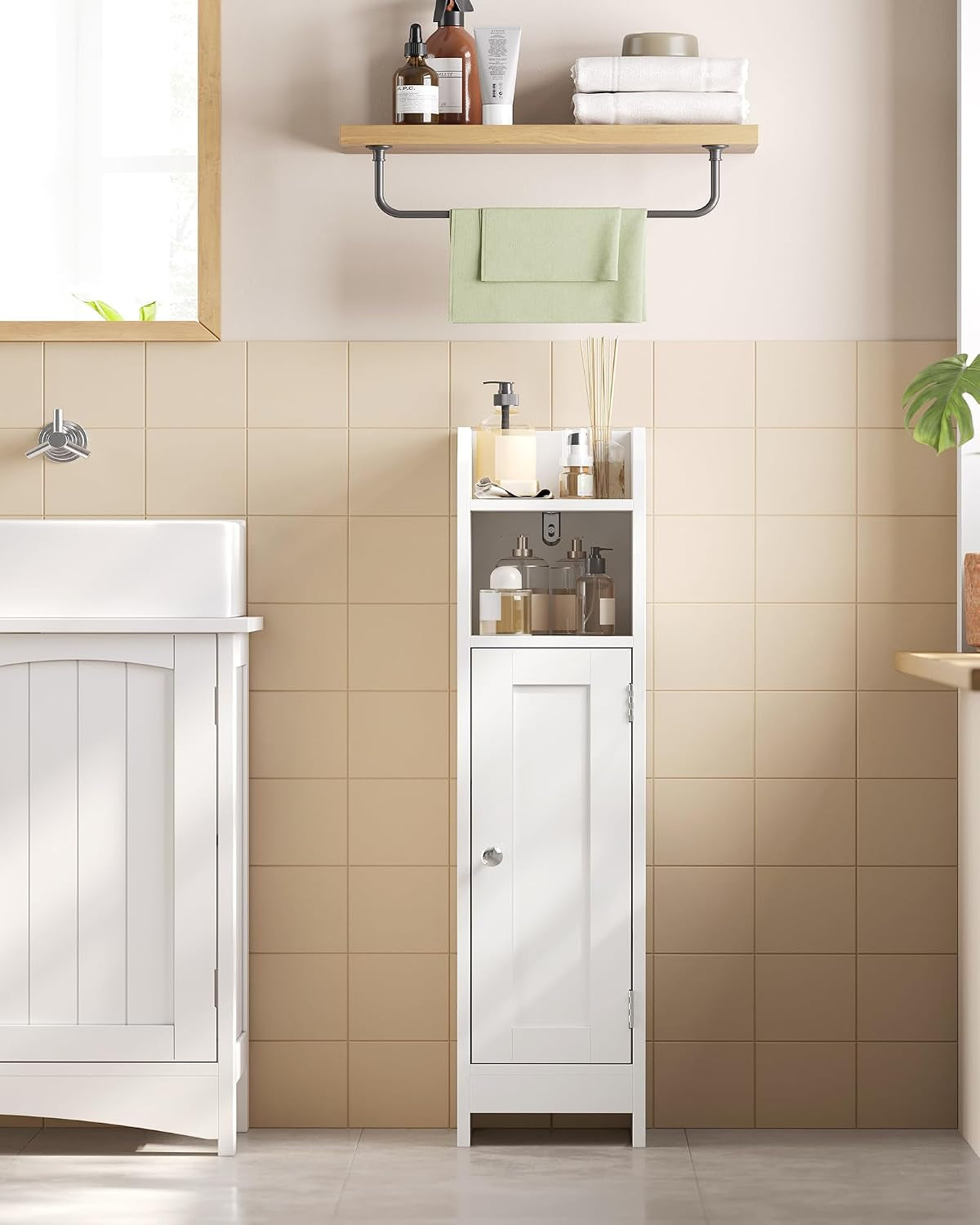 Single slim white bathroom cabinet placed between a sink and wall shelves, stocked with toiletries.