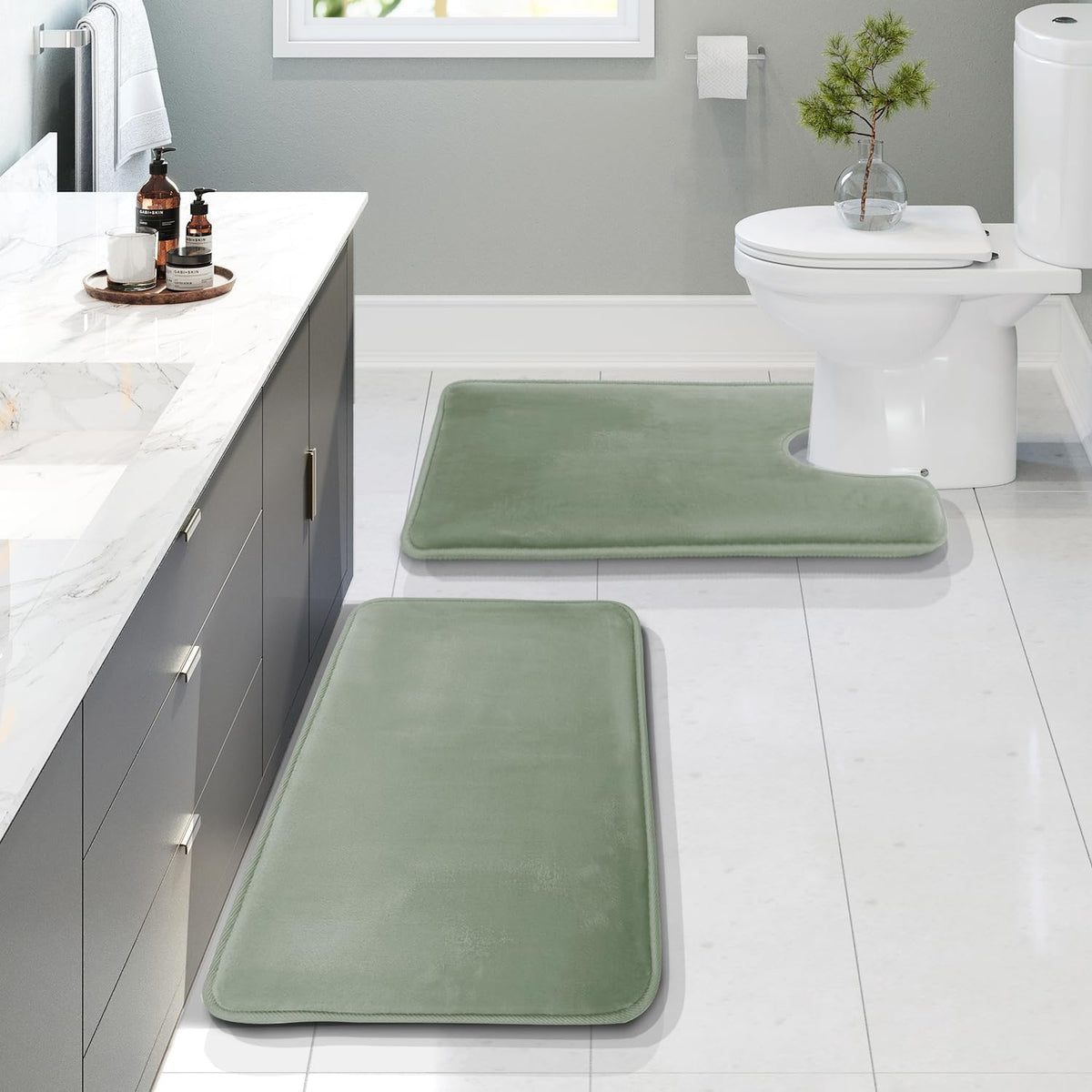 Bathroom view with two sage-green rectangular mats on a tiled floor, one contour mat positioned at the toilet.
