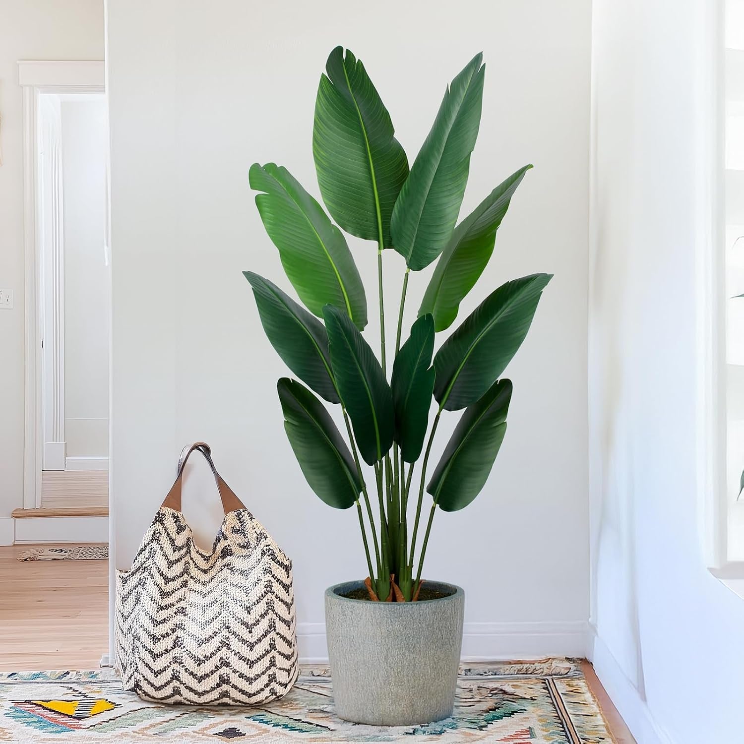 Tall plant in a textured gray planter by a patterned rug with a woven tote bag at its side