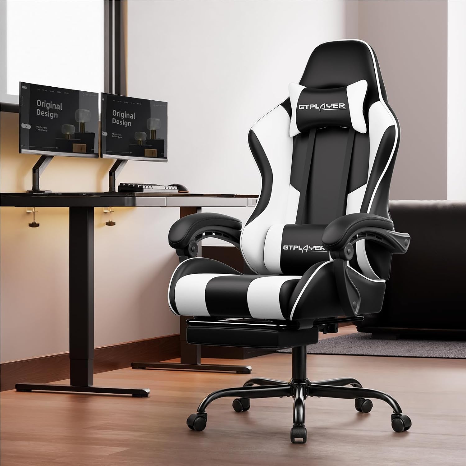 Black and white gaming chair angled front view in a home office setting next to a desk with dual monitors.