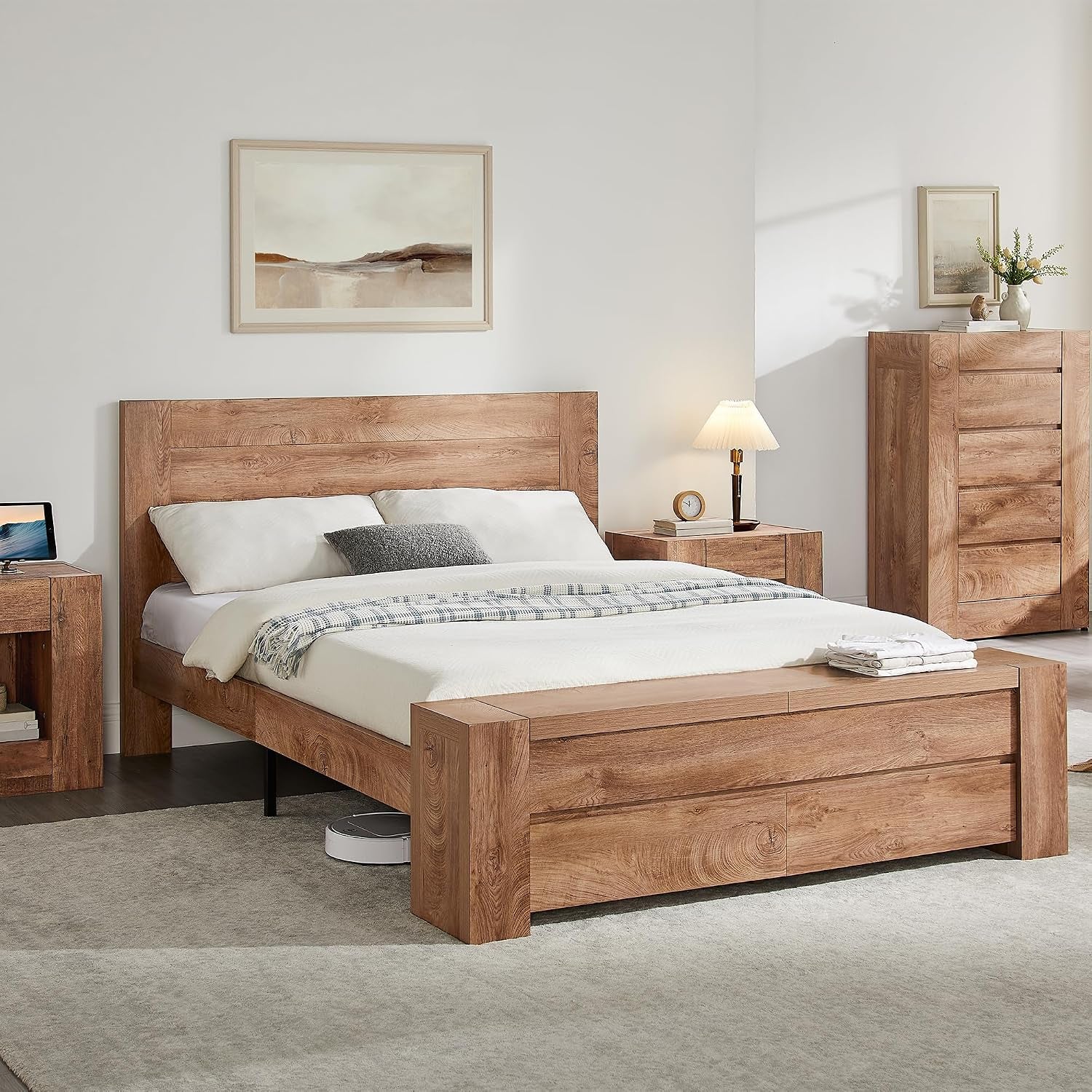 Bedroom scene with a wood-finish platform bed and matching storage bench at the foot, nightstands and tall dresser.