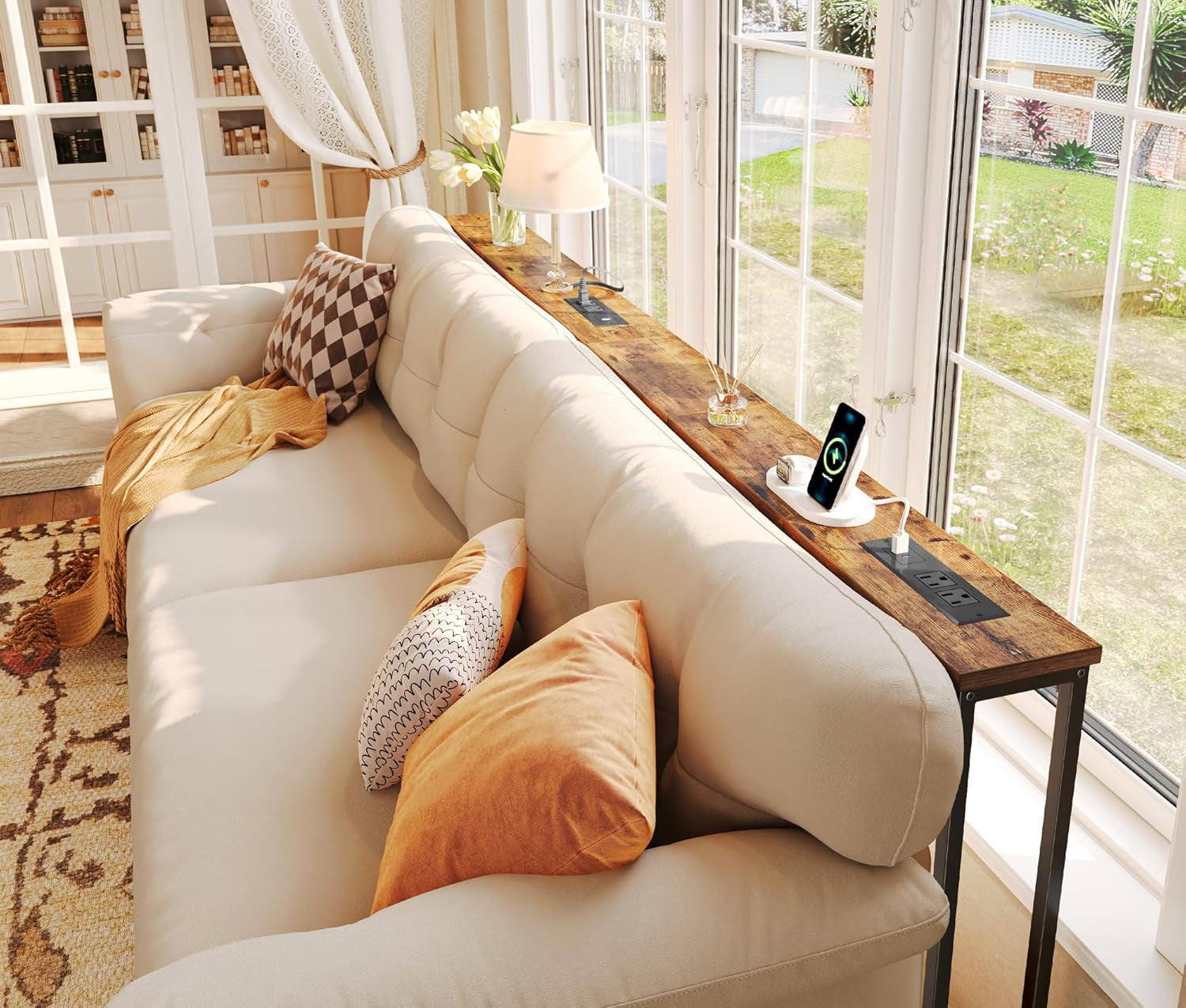 Slim wooden console table behind a cream sofa next to tall windows, showing a phone charging on the tabletop outlet.