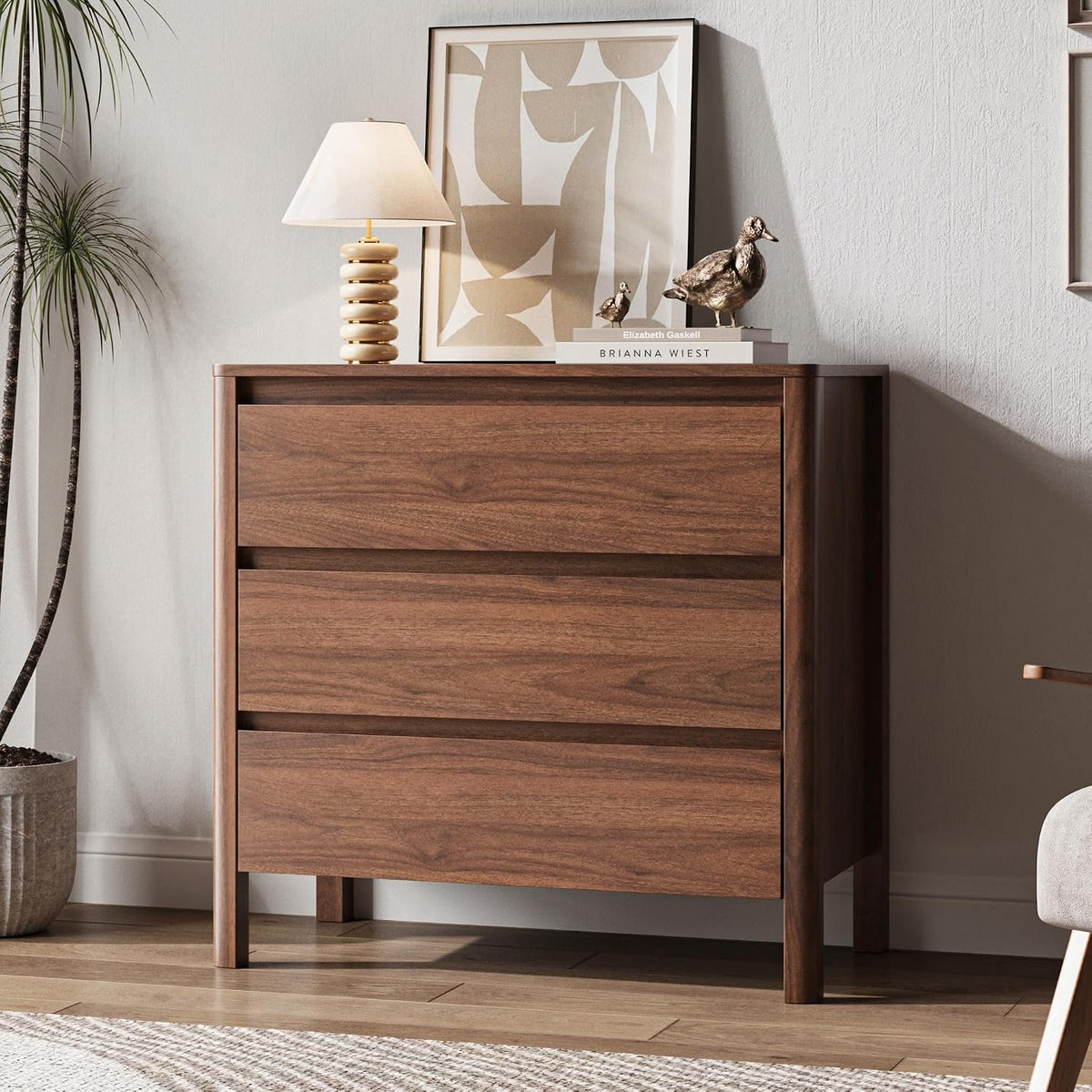Close crop of a three-drawer walnut chest topped with a lamp, stacked books and two small bronze duck figurines.