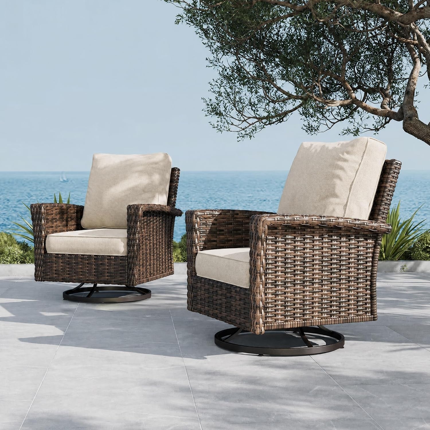 Two brown rattan swivel chairs with beige cushions facing the ocean under a tree.