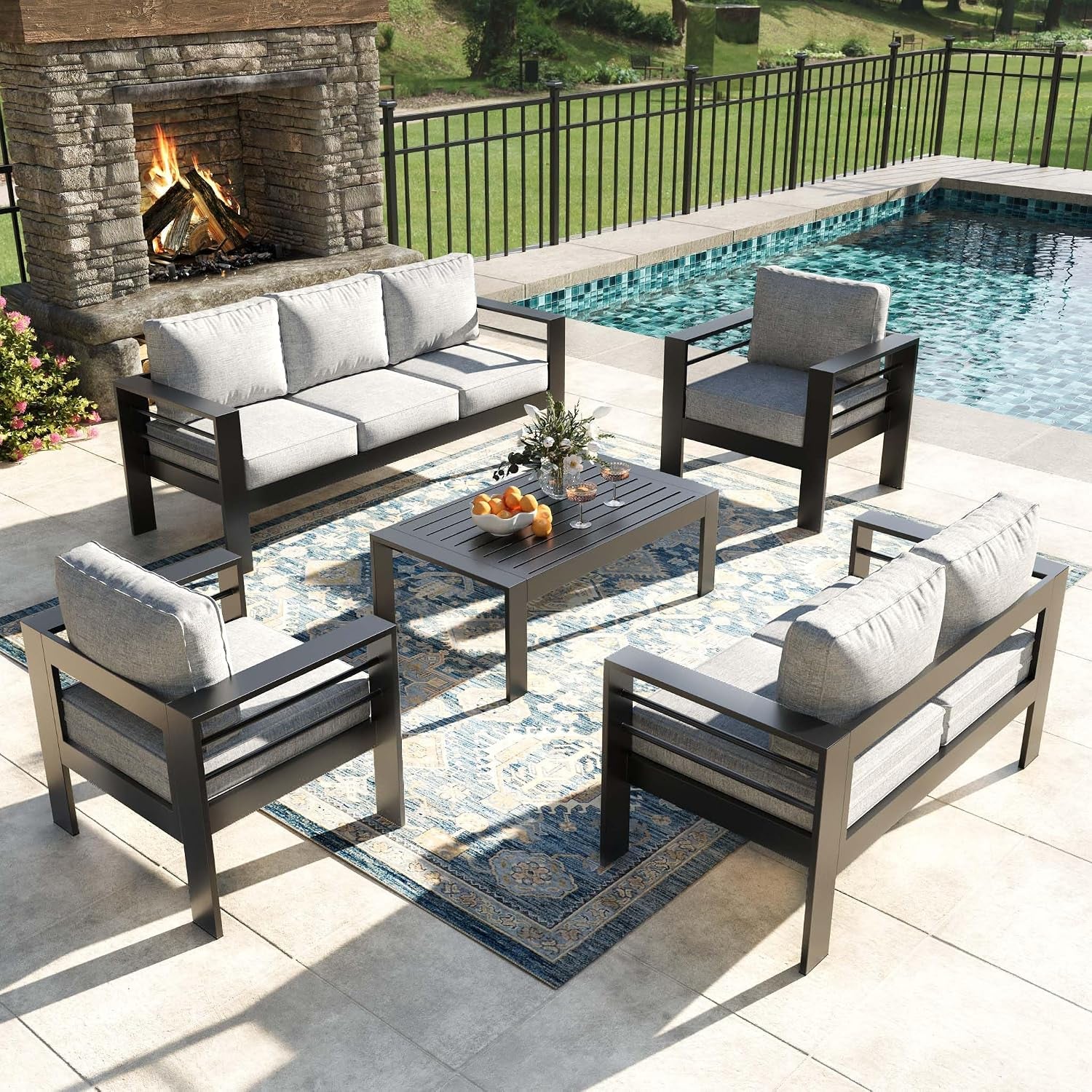 Outdoor aluminum patio conversation set with grey cushions arranged around a slatted coffee table by a pool