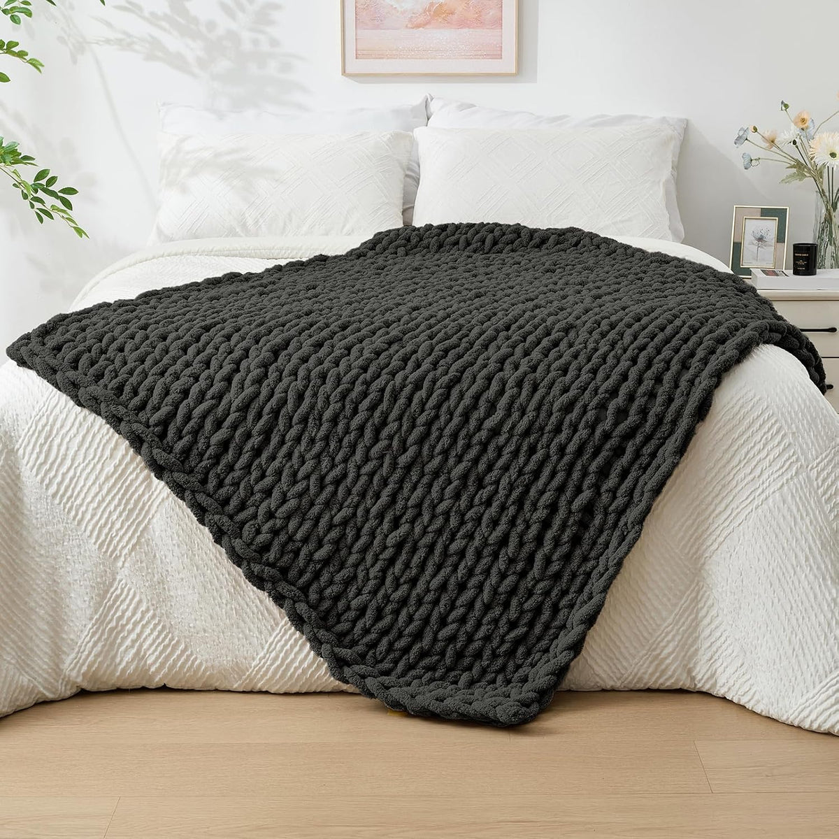 Dark charcoal chunky knit throw spread diagonally across the foot of a white-made bed in a bright bedroom.