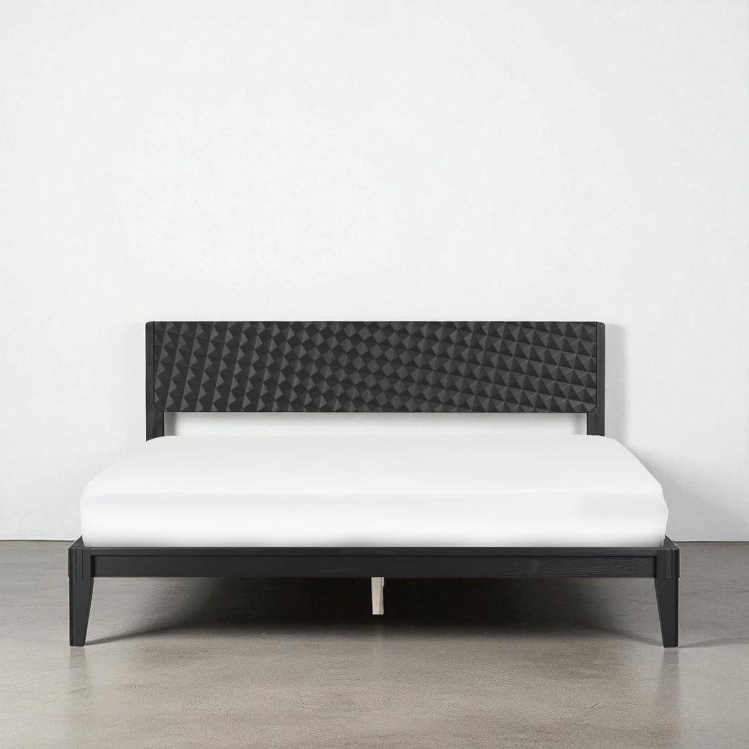 Low front view of the queen bed in a deep black finish on a polished concrete floor.