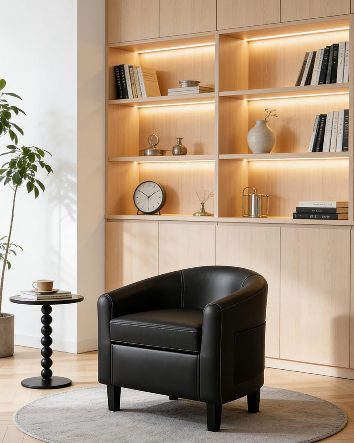 Black barrel chair placed on a round rug in front of lit wooden shelving and a side table.