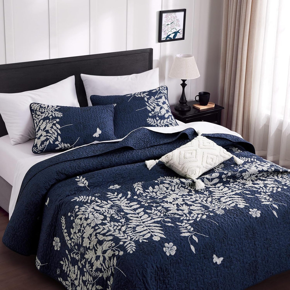 Angled view of navy floral quilt with two matching pillow shams and a tasseled decorative pillow on the bed