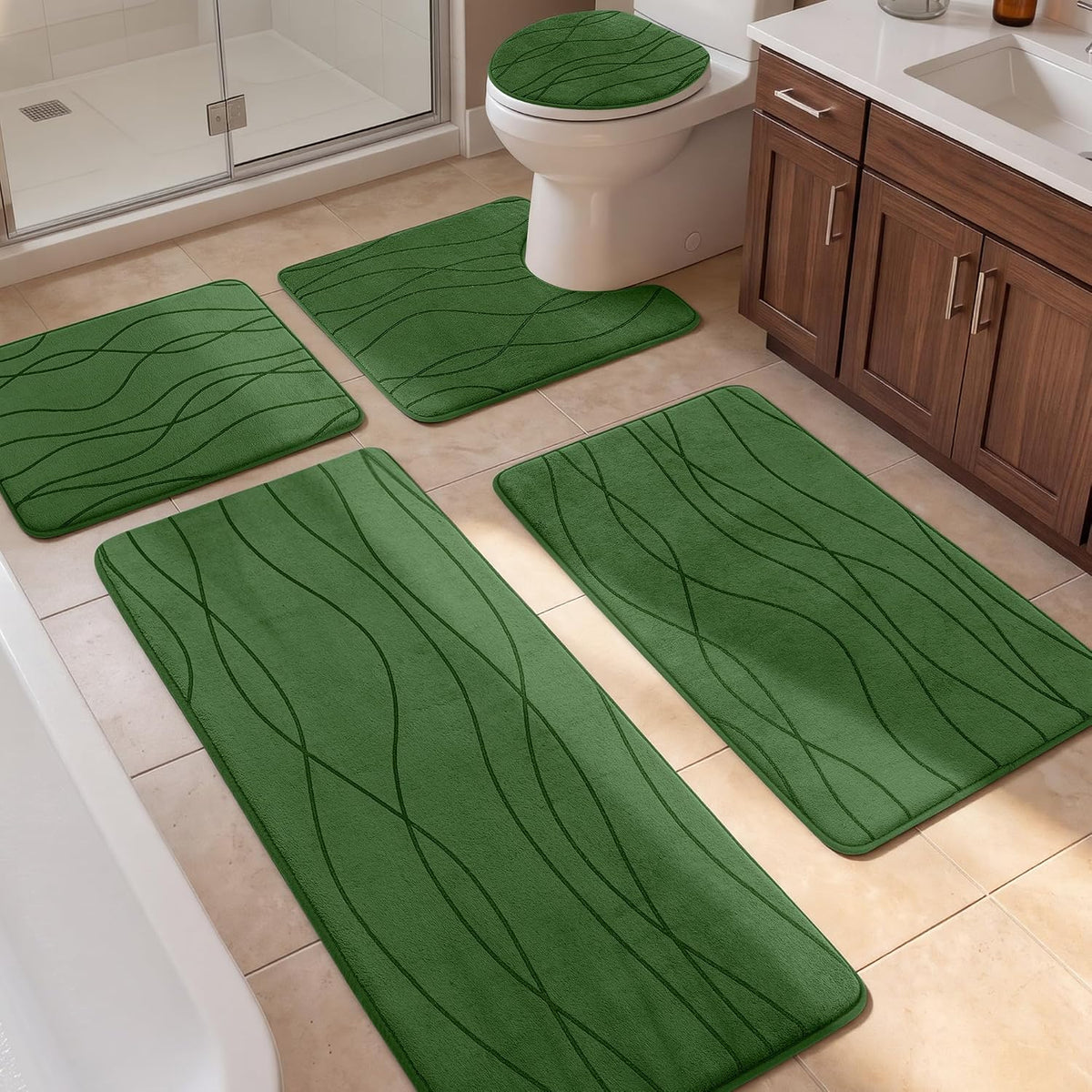 Five green bathroom rugs including a toilet lid cover and four floor mats on beige tile near shower and vanity.