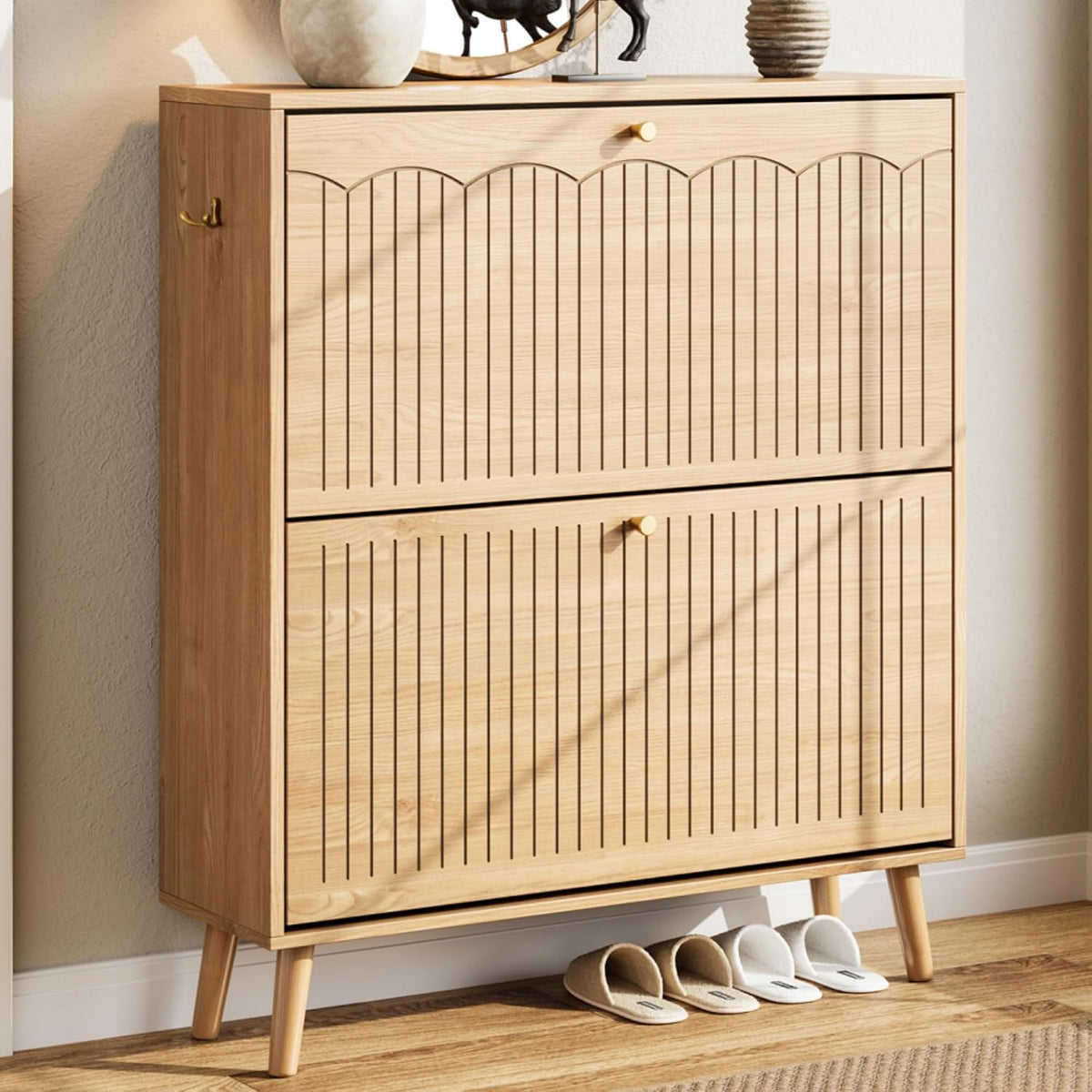 Side-angled view of a mid-century style light wood shoe cabinet on tapered legs with vertical grooved drawer fronts