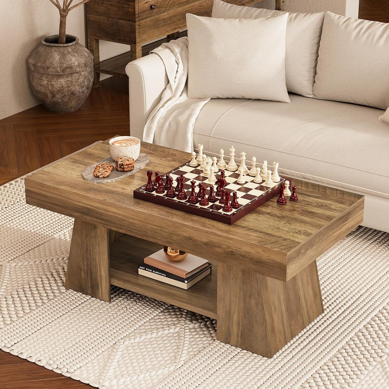 Coffee table beside a beige sofa on a textured rug, topped with a chessboard, cup and cookies; lower shelf holds books and