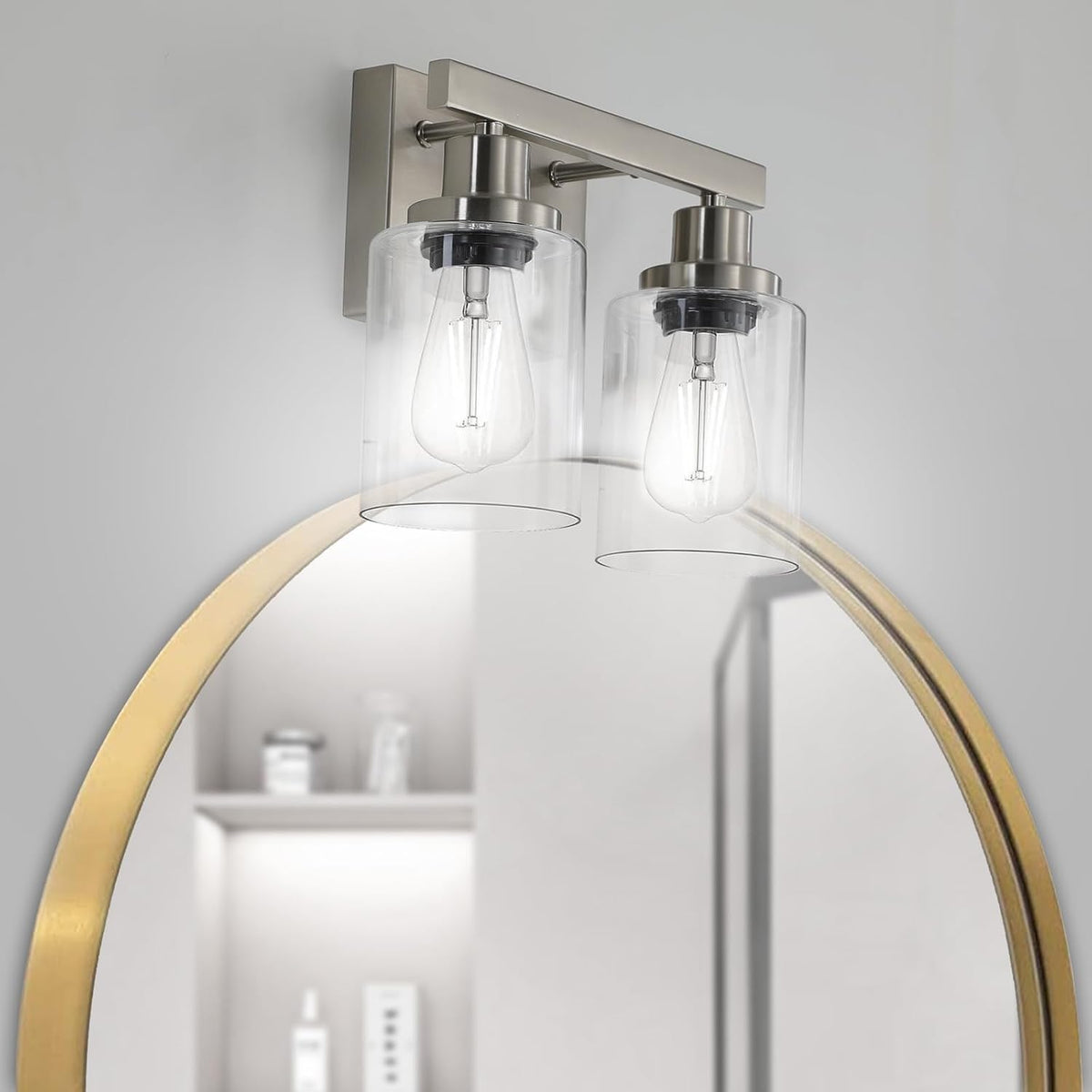 Two-light brushed nickel vanity light with clear glass shades mounted over a round mirror edge.