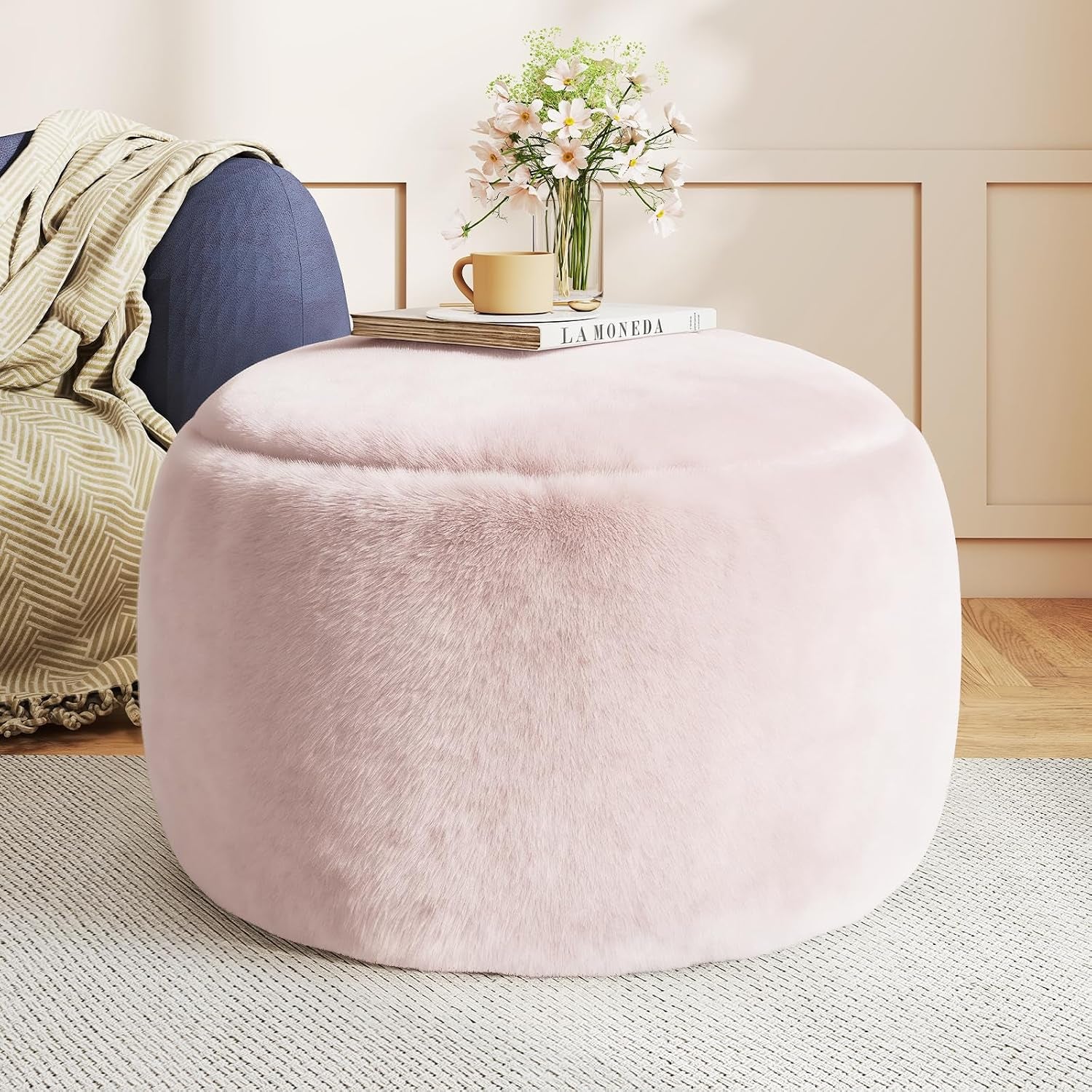 Pink round faux-fur pouf ottoman with book and vase on top beside a sofa