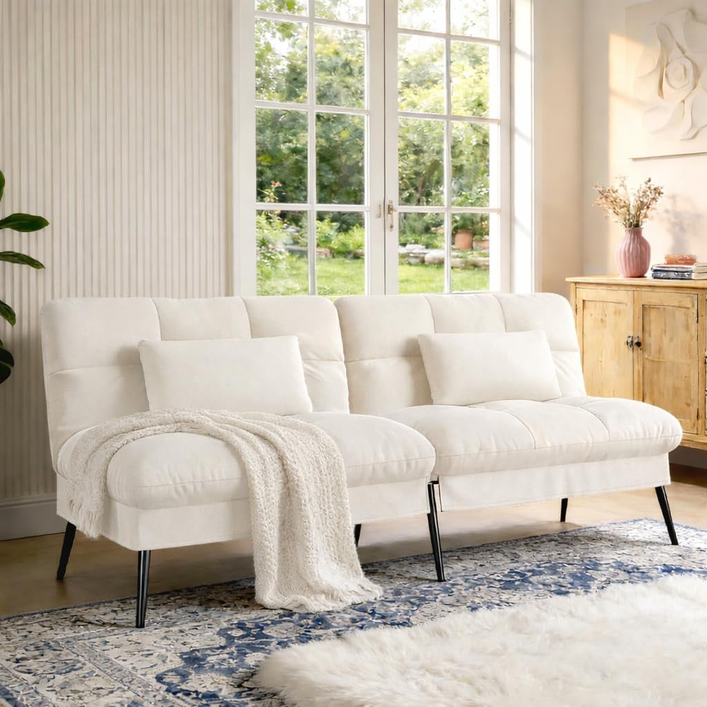 Cream/ivory fabric futon sofa with lumbar pillows and a knitted throw in a bright room by French doors.