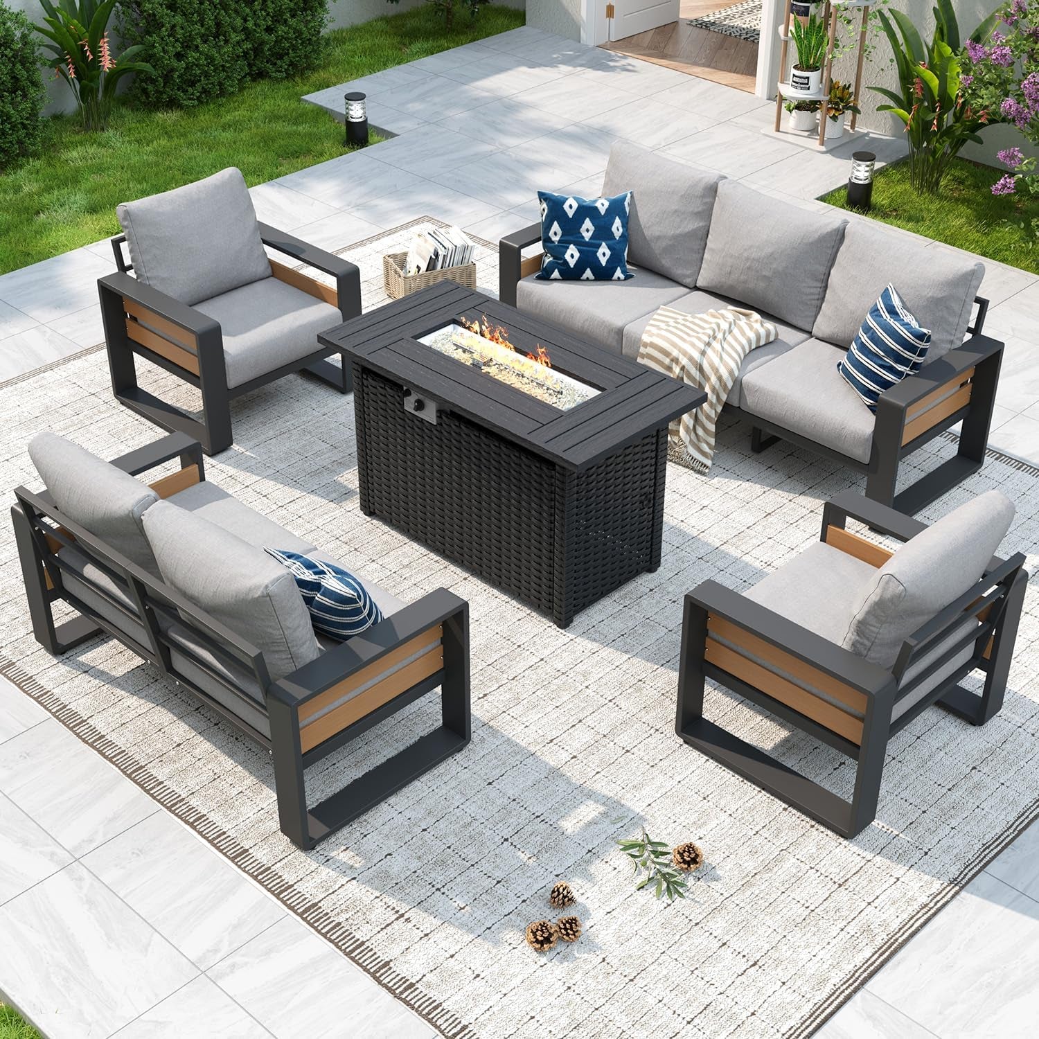 Outdoor sectional arranged around a rectangular fire-pit table on a light rug, charcoal frame and gray cushions.