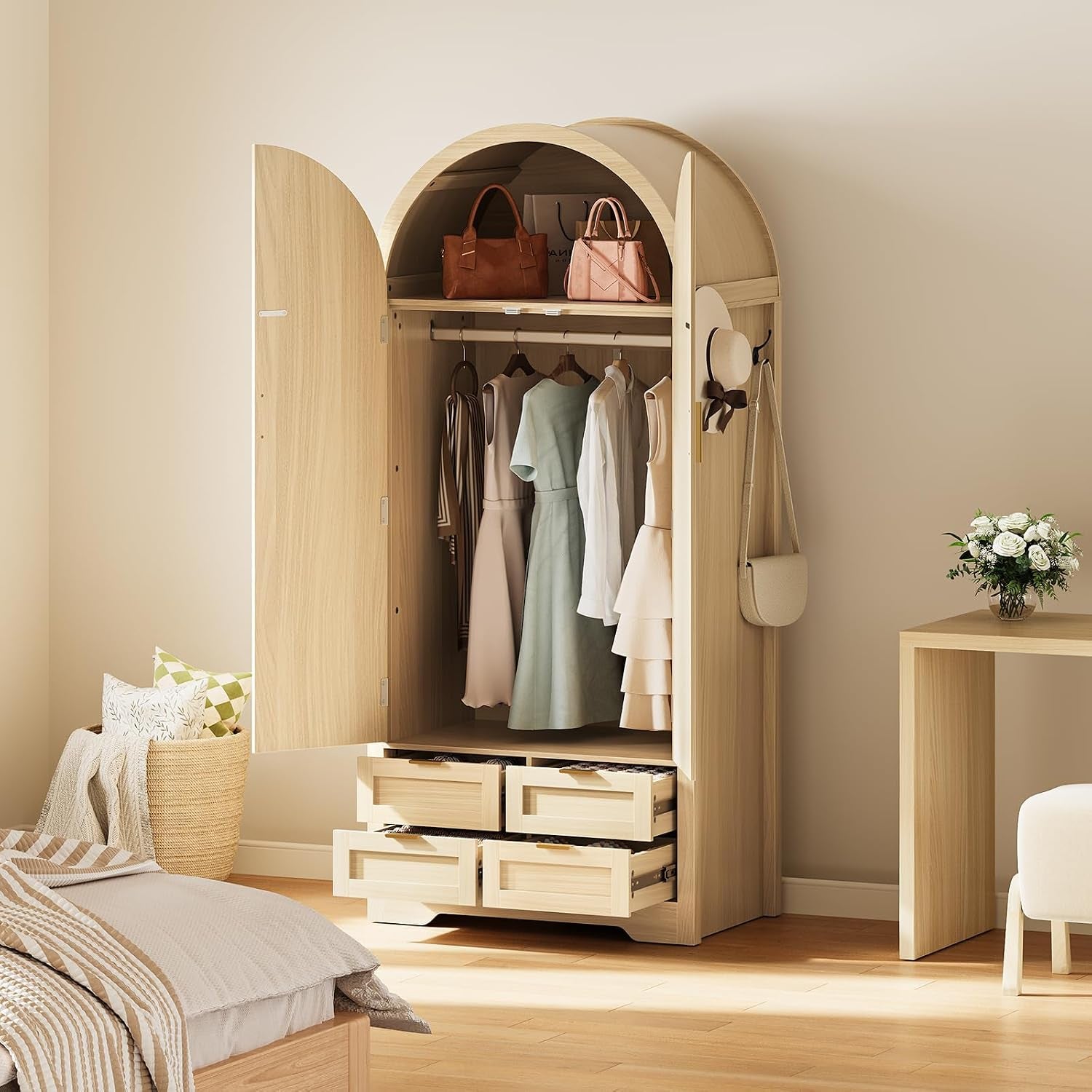 Open arched wooden wardrobe in a bedroom with hanging clothes, top shelf bags and four lower drawers partly open.