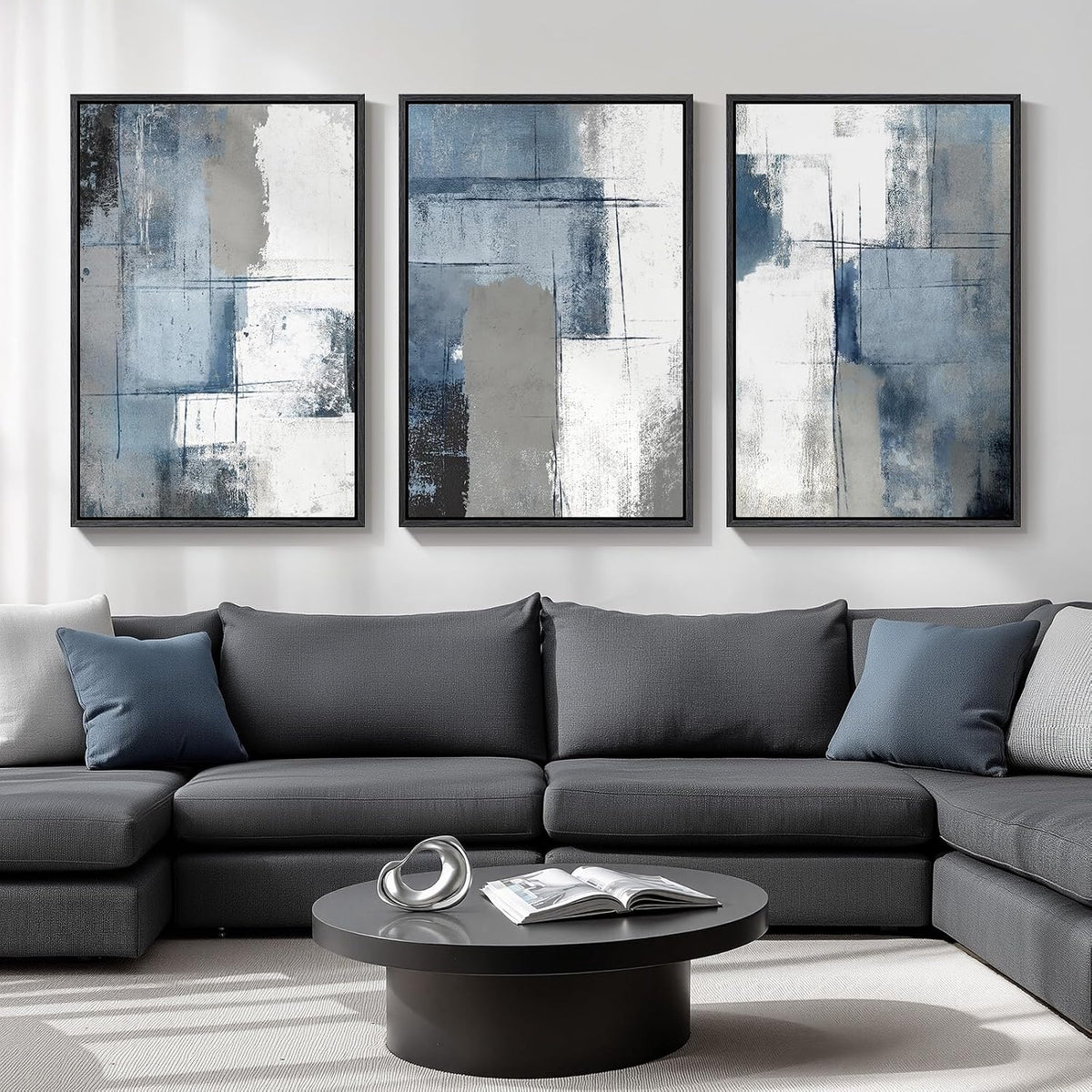 Three vertical blue-gray abstract framed prints hung above a dark gray sectional in a living room.