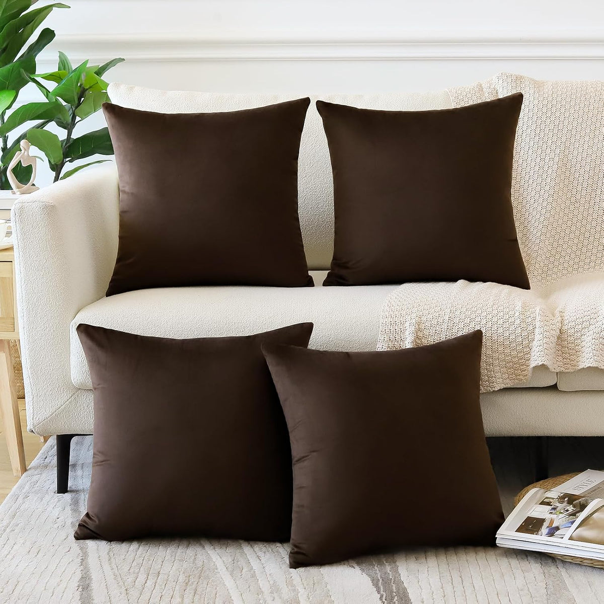 Four square velvet pillow covers in dark brown arranged on a white sofa with a knit throw