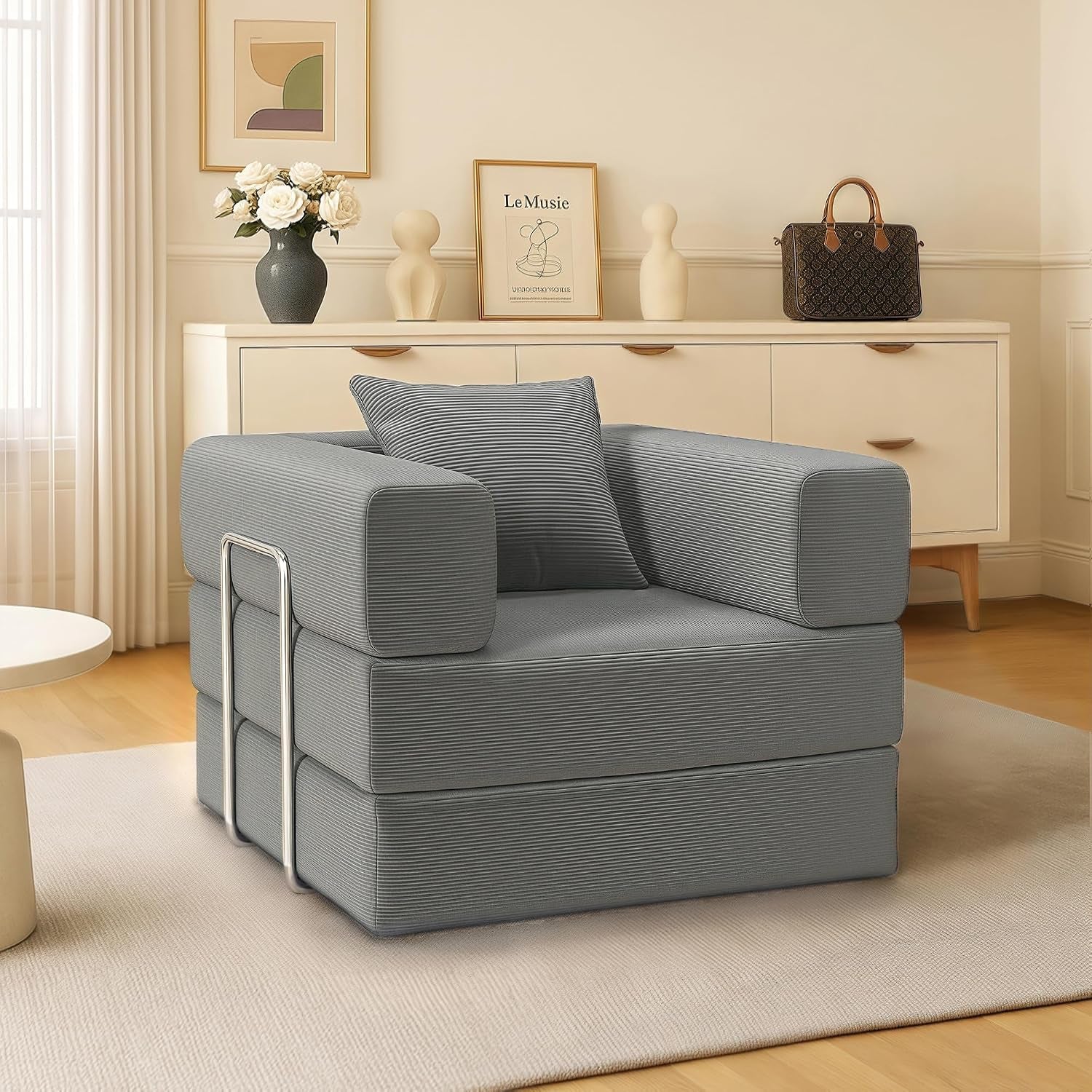 Angled side view of a gray corduroy two-seat convertible floor sofa with chrome side rails in a living room.