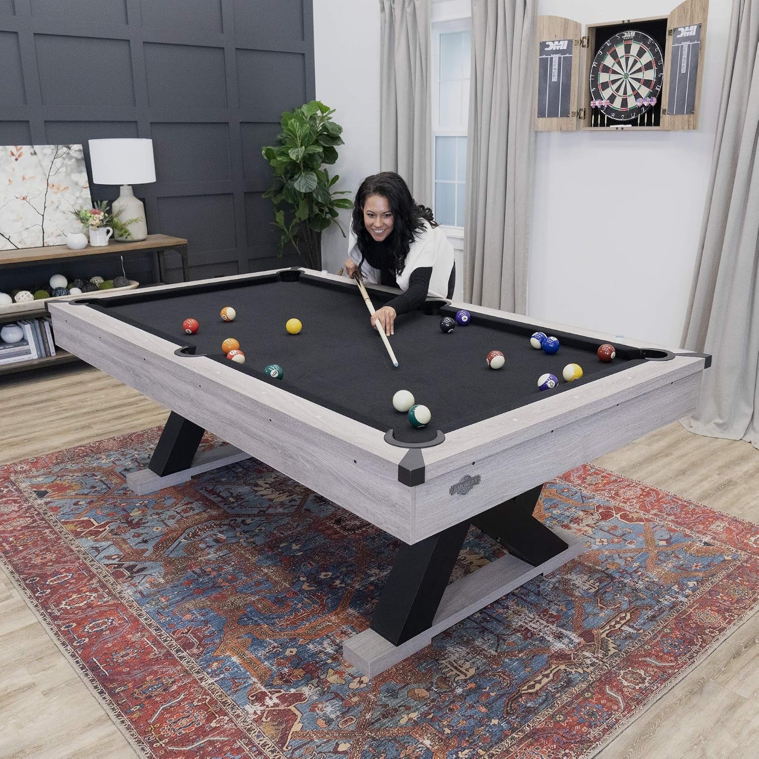 Person leaning over the billiard table taking a shot with balls scattered on the black surface and K-shaped legs visible.