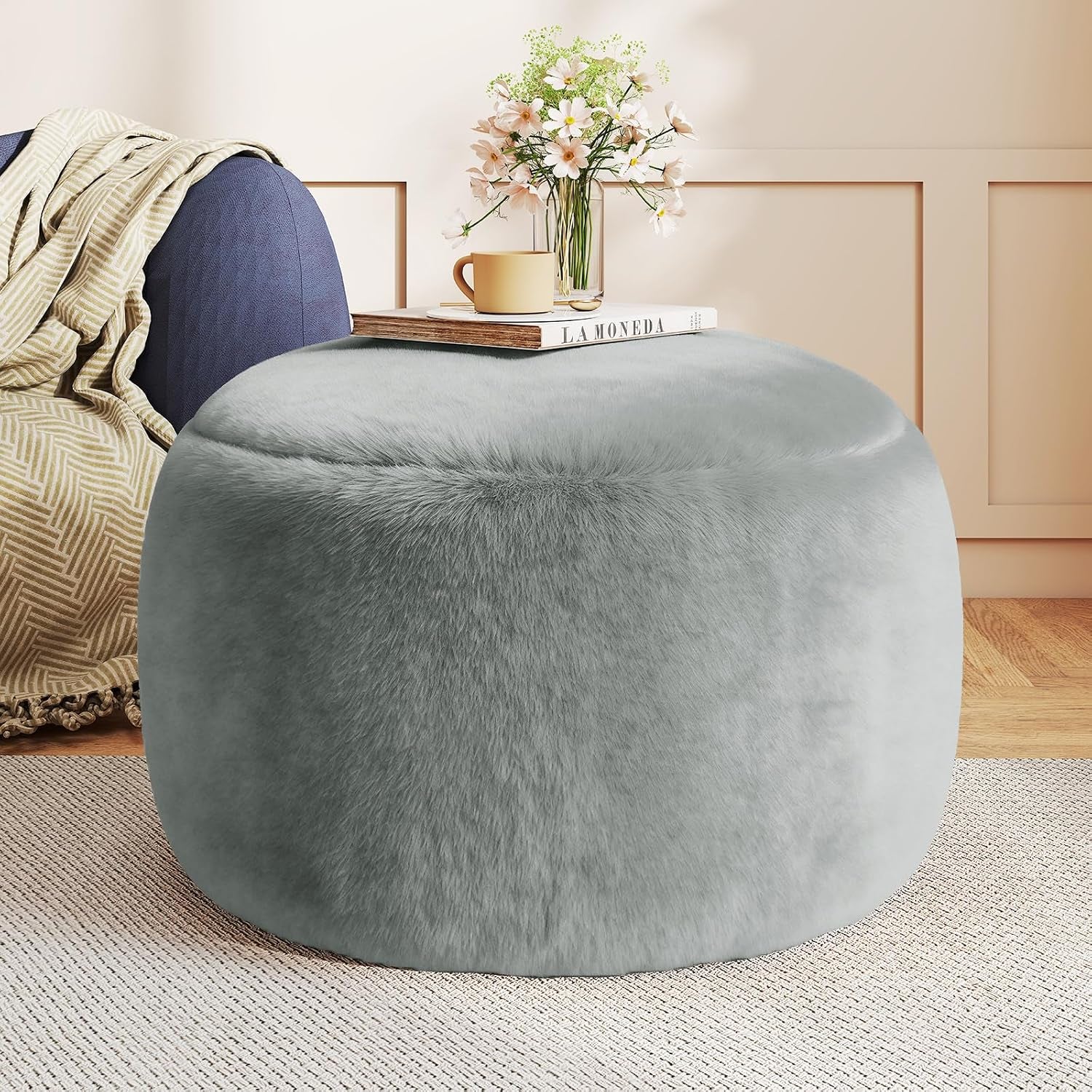 Light grey faux-fur round pouf ottoman front view with book and vase on top